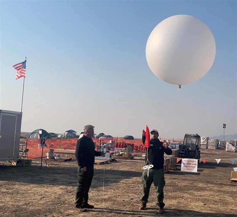 A large white balloon with small equipment attached to a long string is let go so it can fly thousands of feet and assist with weather forcasts