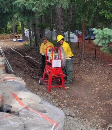 Two crew members are using a hose roller to repack miles of fire hose that's been cleaned