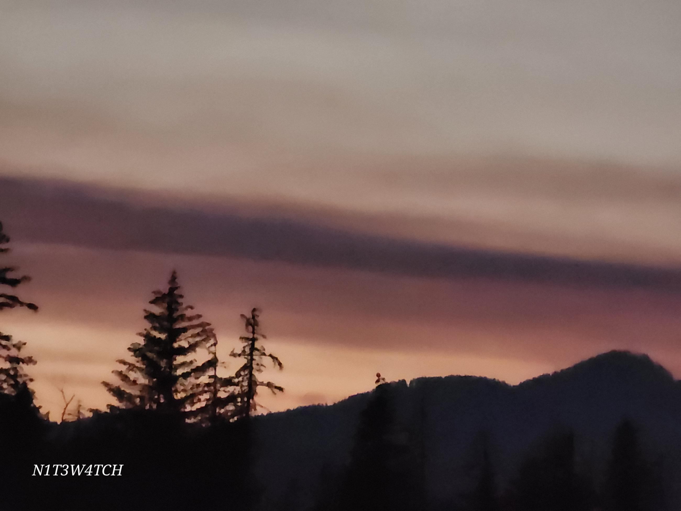 image of smoke at sunset with silhouetted trees and mountains. 