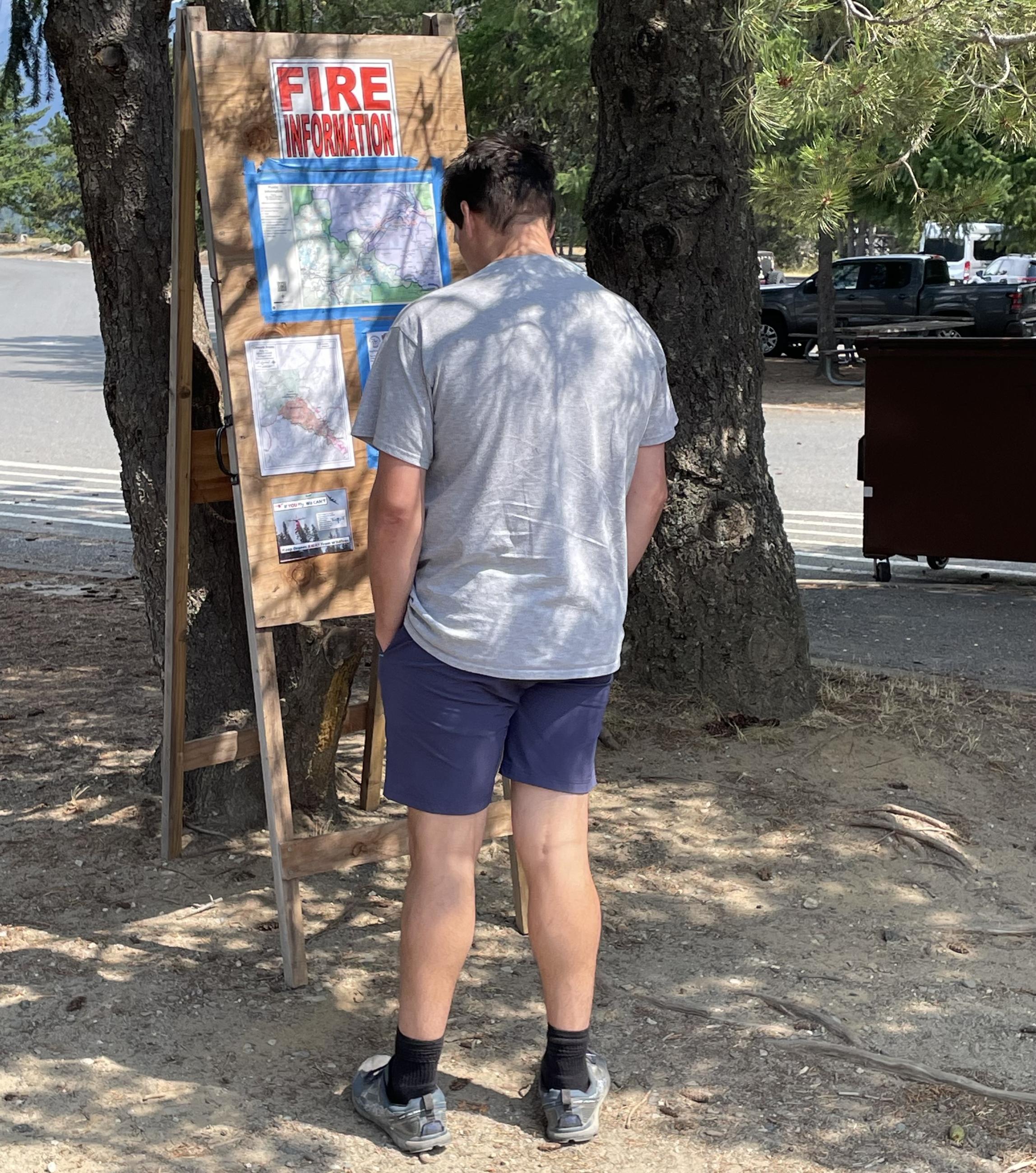 A visitor studies Fire Information maps and info posted on a wooden A-frame display at Diablo Lake Overlook