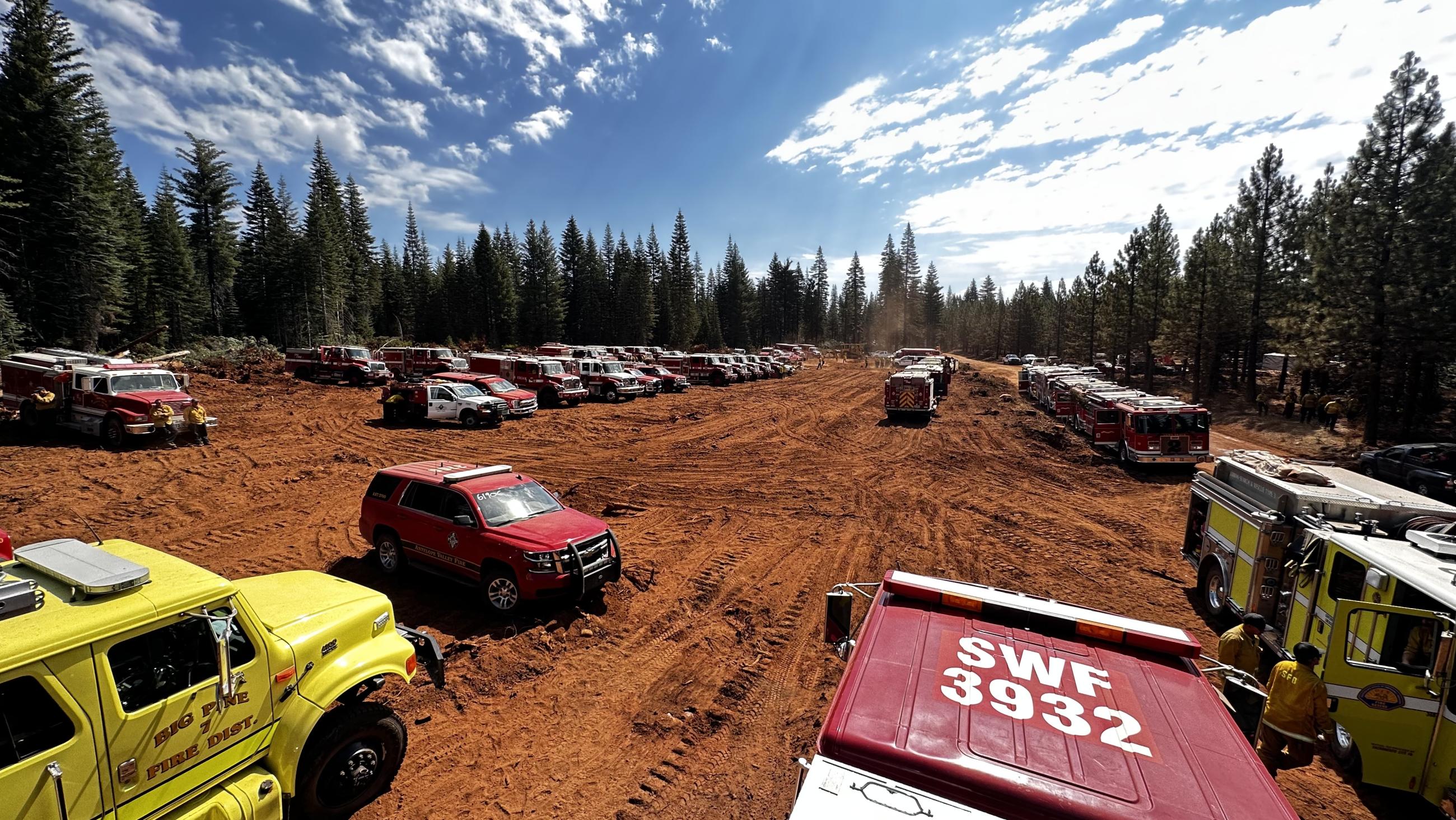 Dozens of fire engines and other vehicles park in a dusty area waiting for assignement