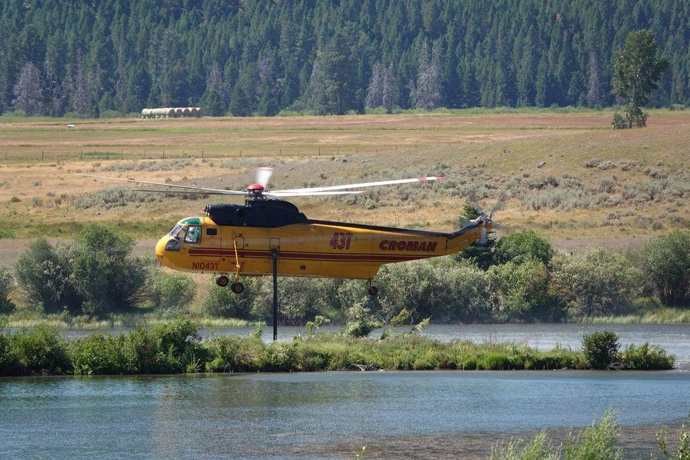 Large single rotor helicopter hovering above a lake using a snorkel to fill its tank