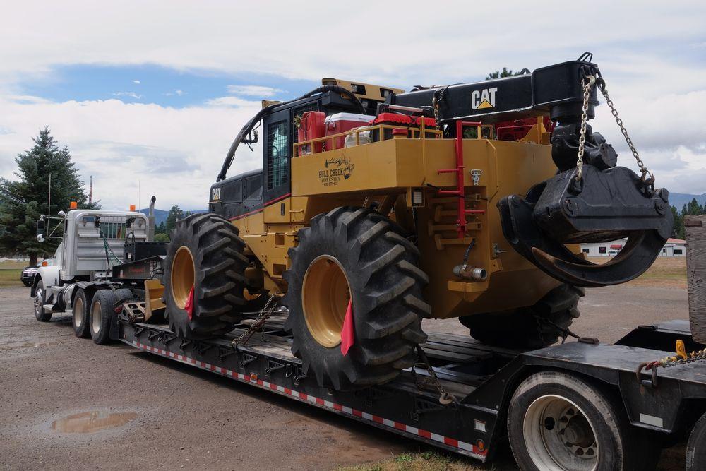 Large piece of wheeled machinery on a lowboy trailer behind a semi tractor