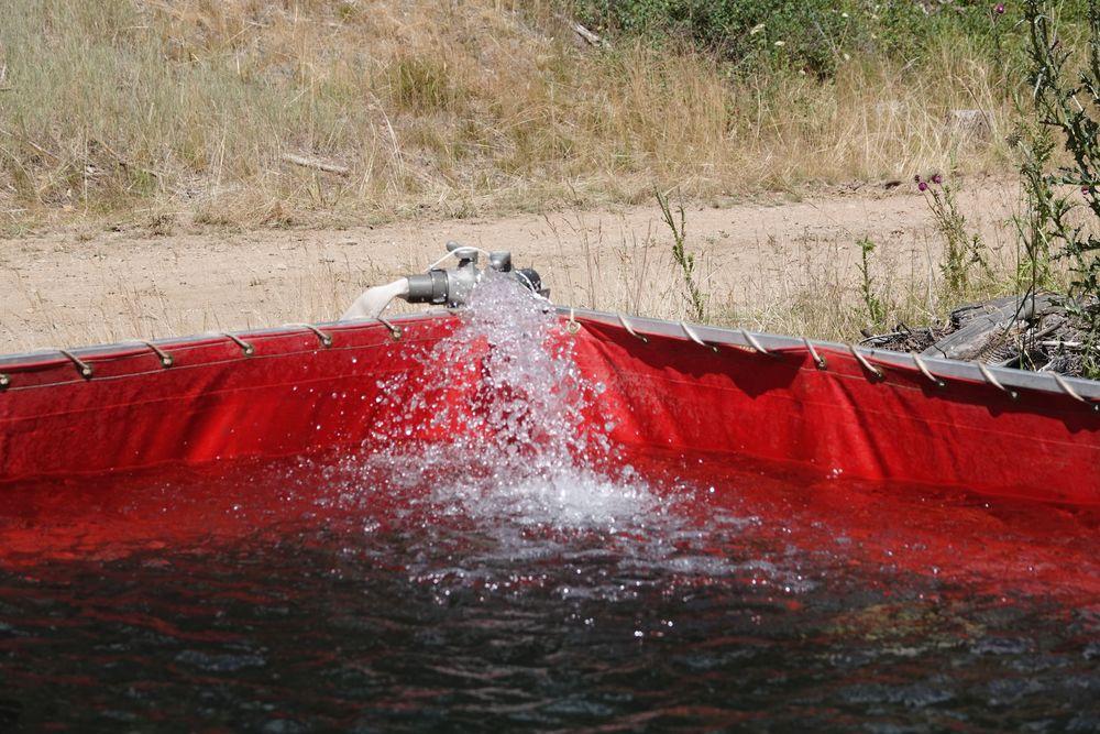 Corner of red frame supported water tank with hose and fitting and flowing water