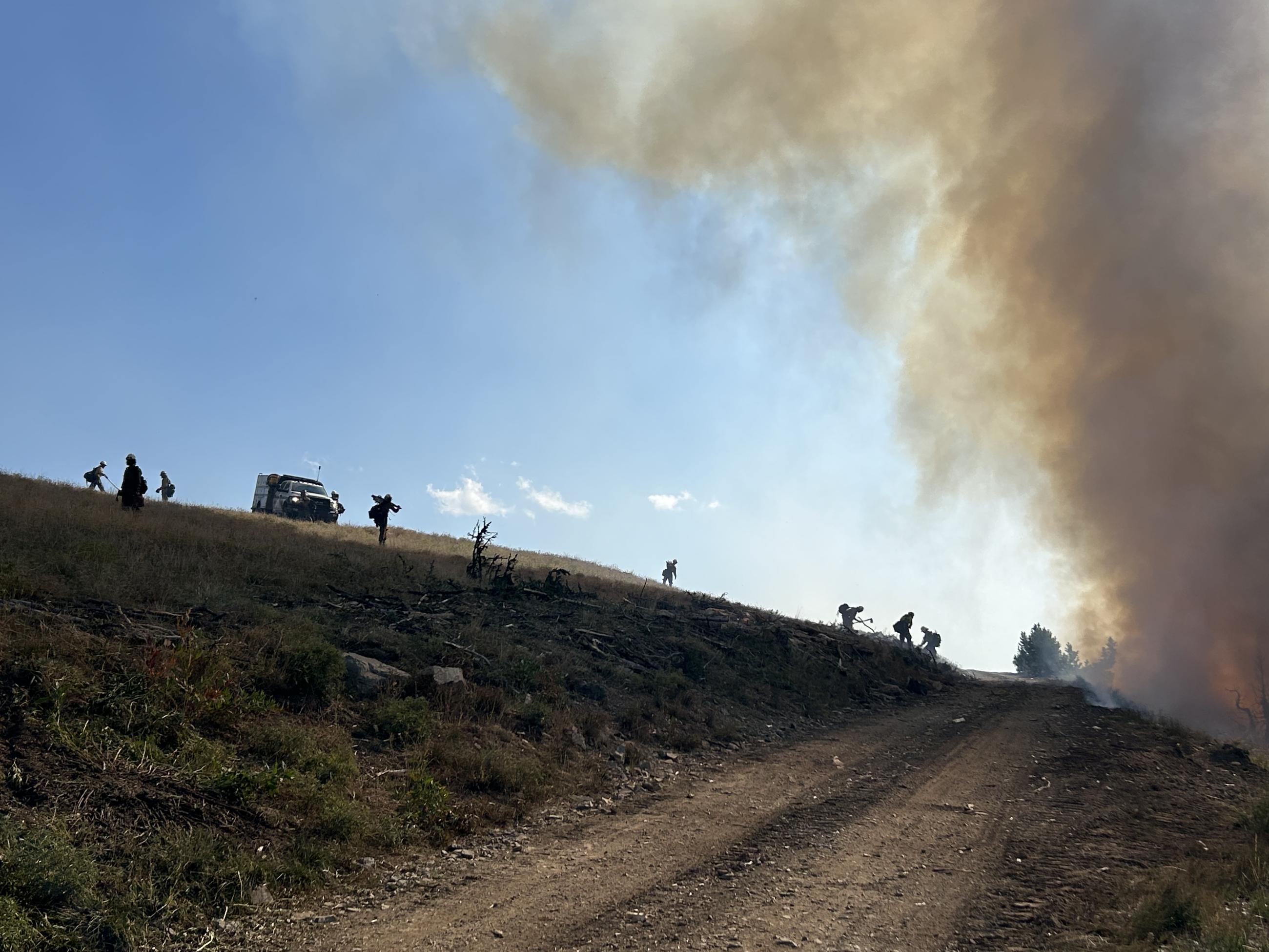 road with firefighters and smoke in background