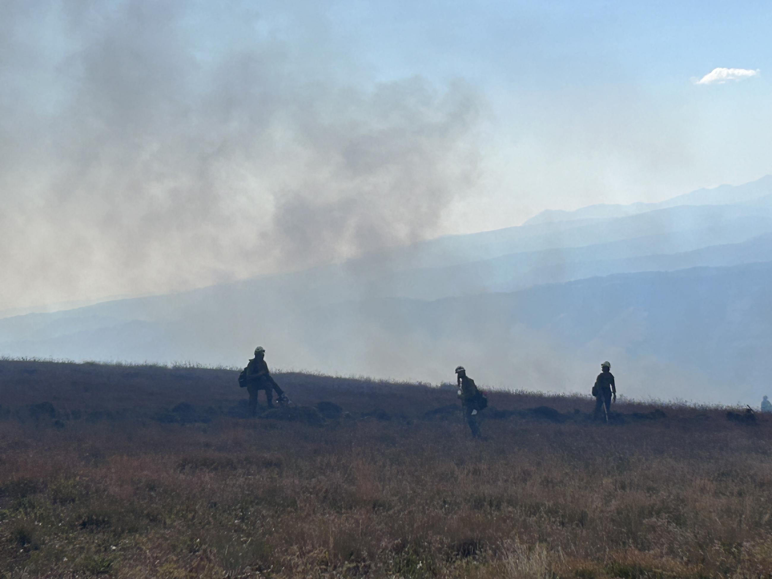 three firefighters with smoke in background