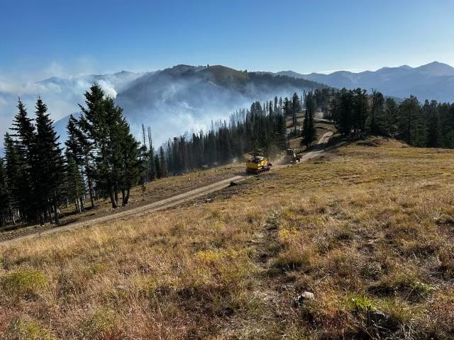 grader driving on road with smoke in the background