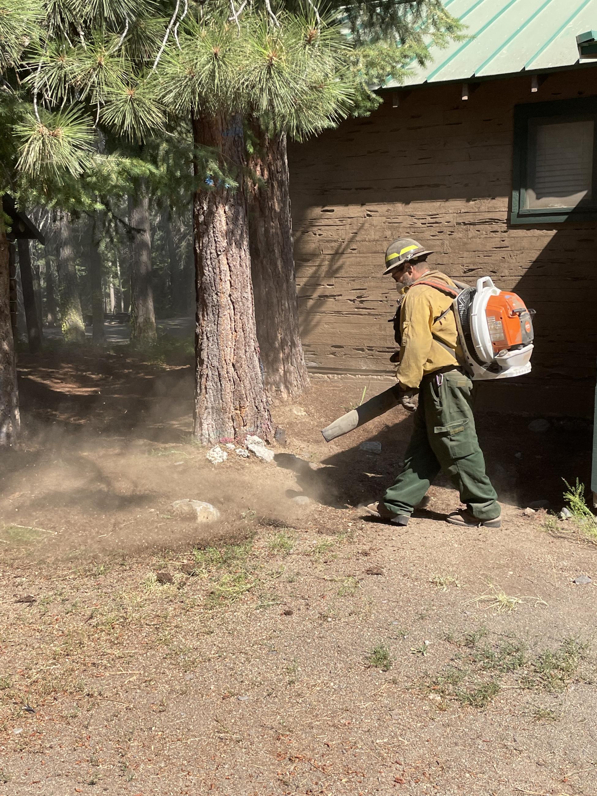 Firefighter works with a backpack blower to blow needles away from a structure.