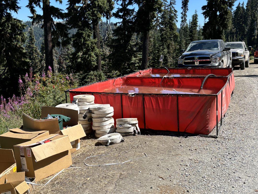 Picture of 2 large orange portable tanks full of water. Hose rolls lie next to the tanks.