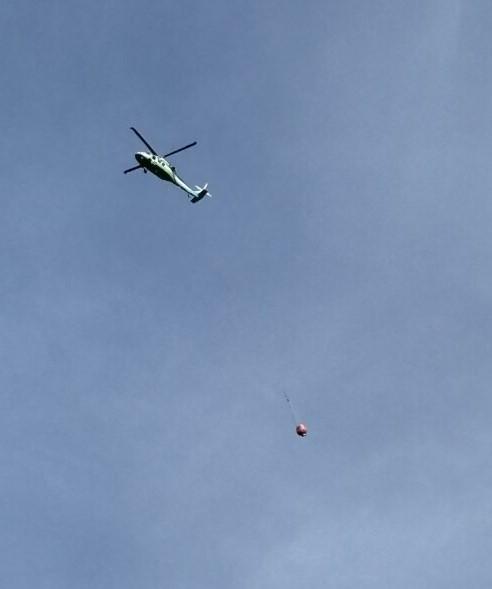 A helicopter with a long line bucket underneath, ready to drop water on the fire area.