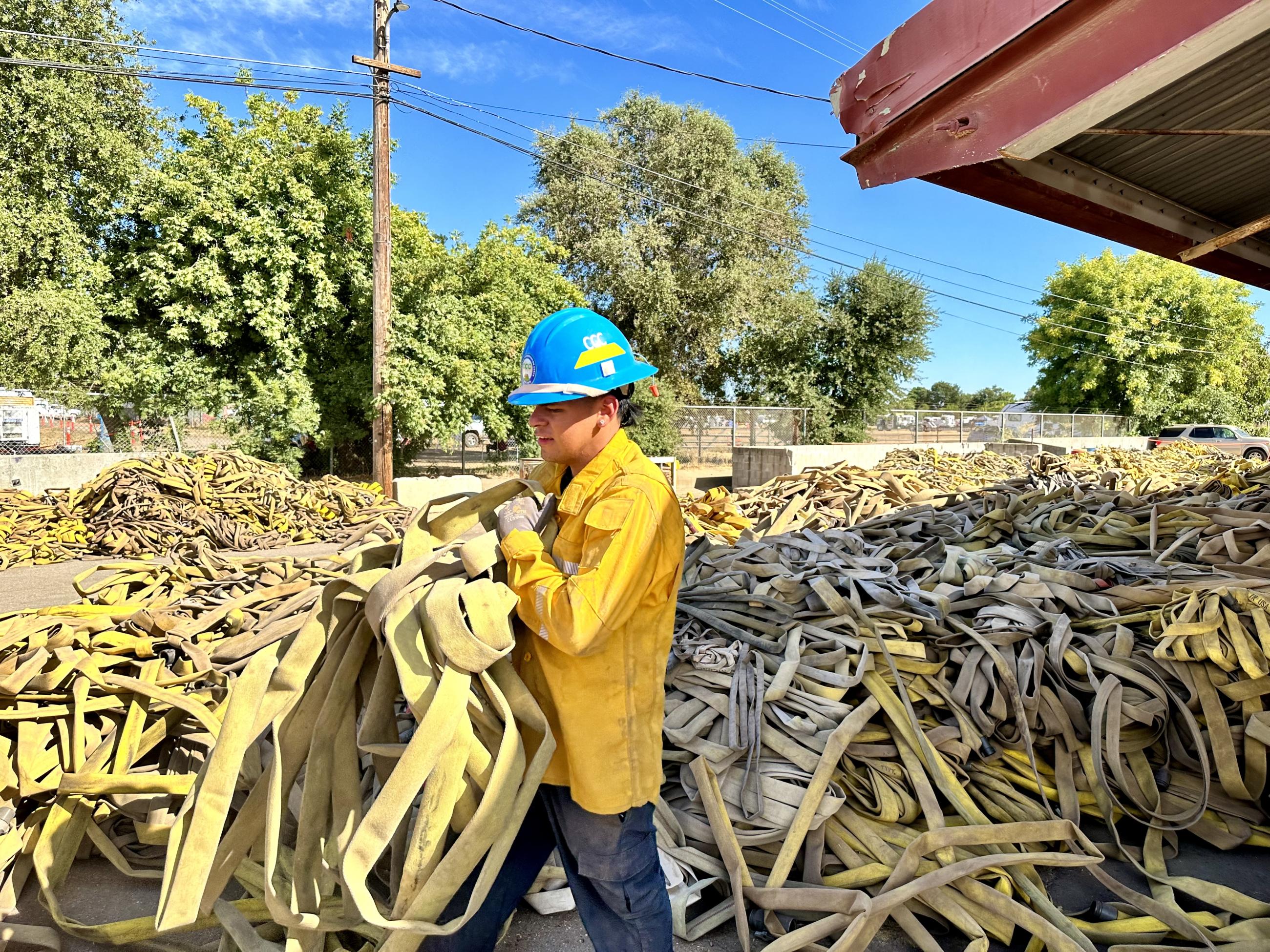 a worker carries a tangle of fire hose Fire Hose to be Sorted, Cleaned, Rolled and Packed for the Next Fire, 8-19-2024