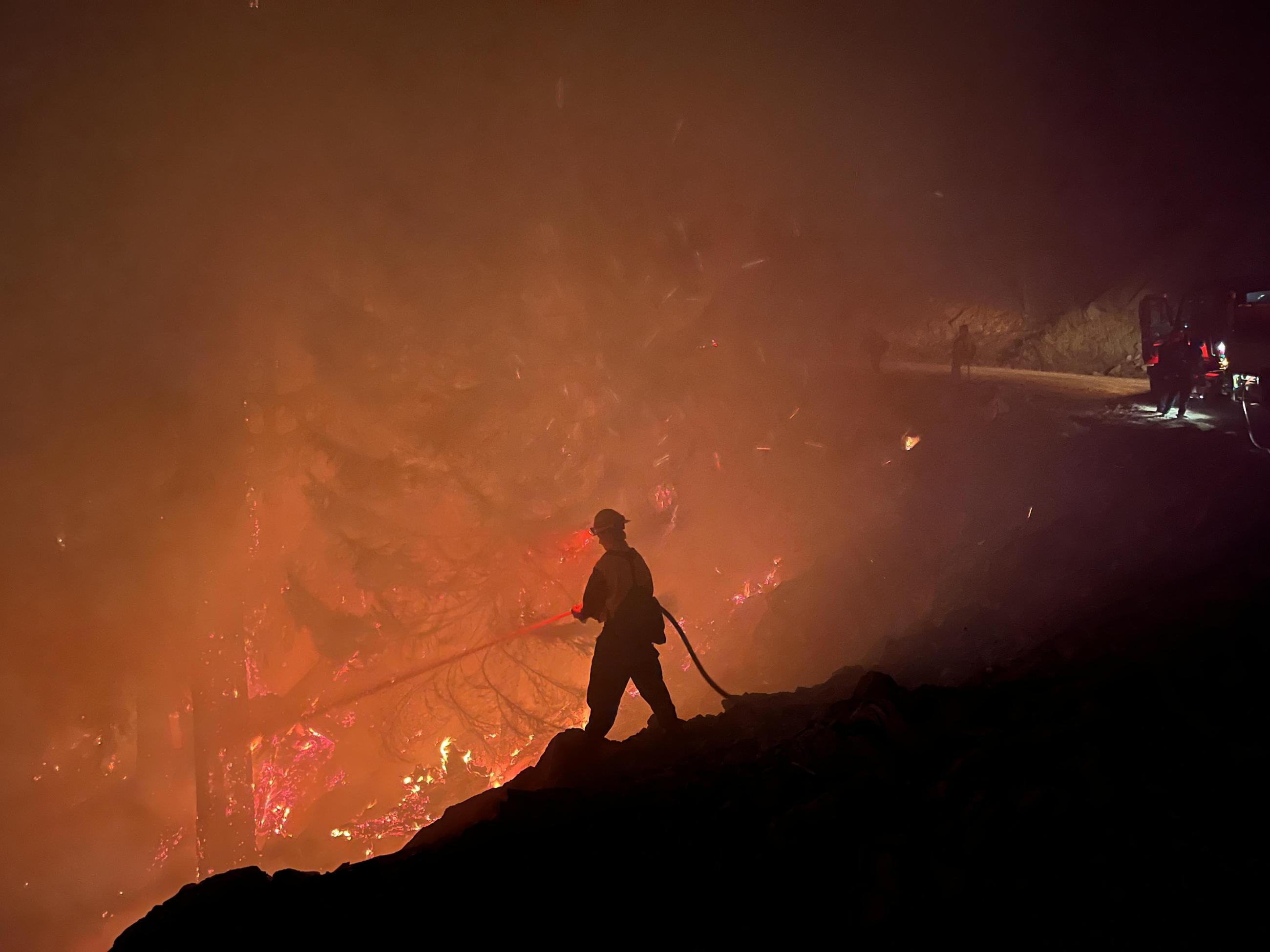 A firefighter silhouetted against fire glow.