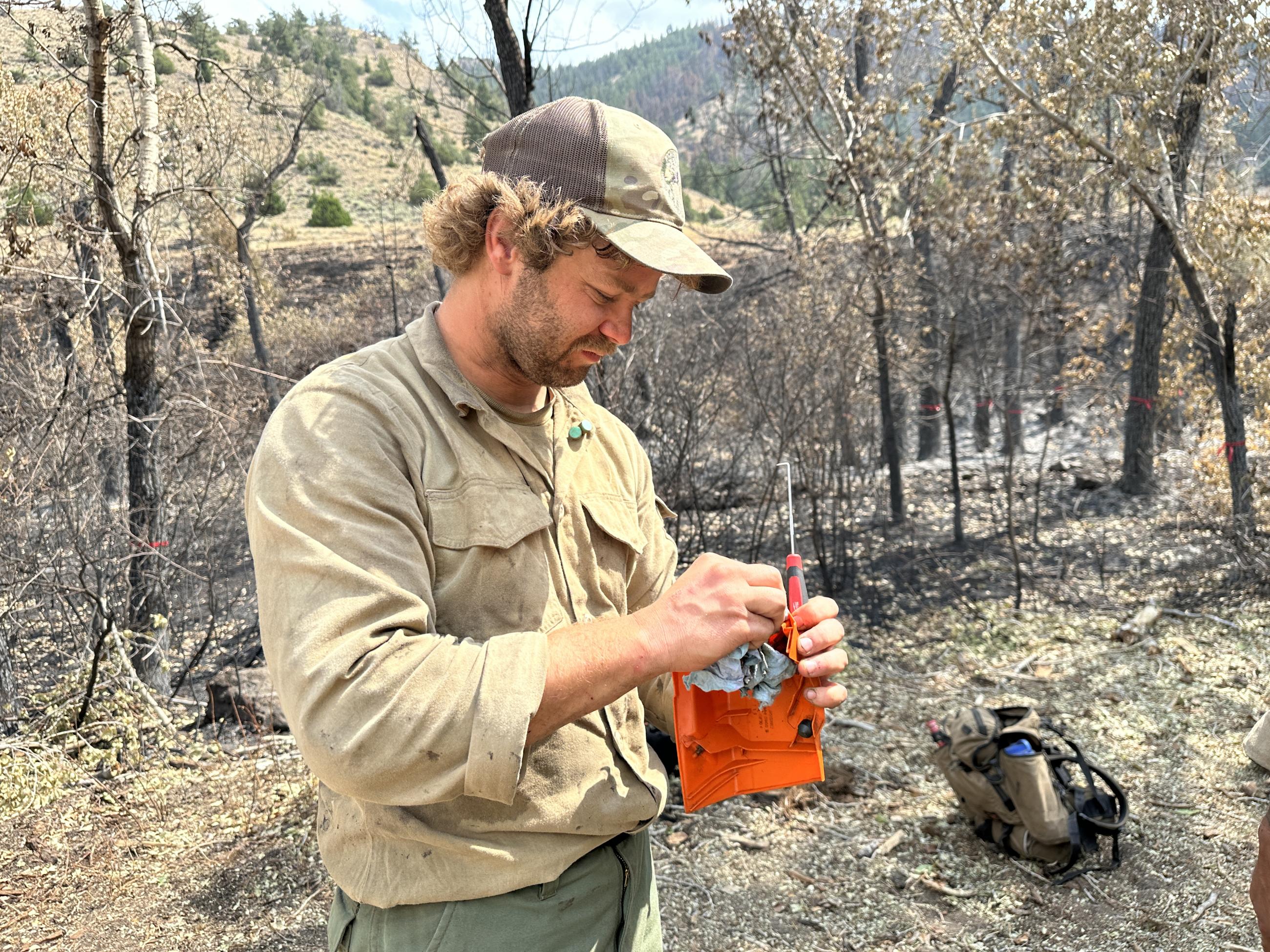 A firefighter holds an orange plastic piece that is part of a cover for a chainsaw.