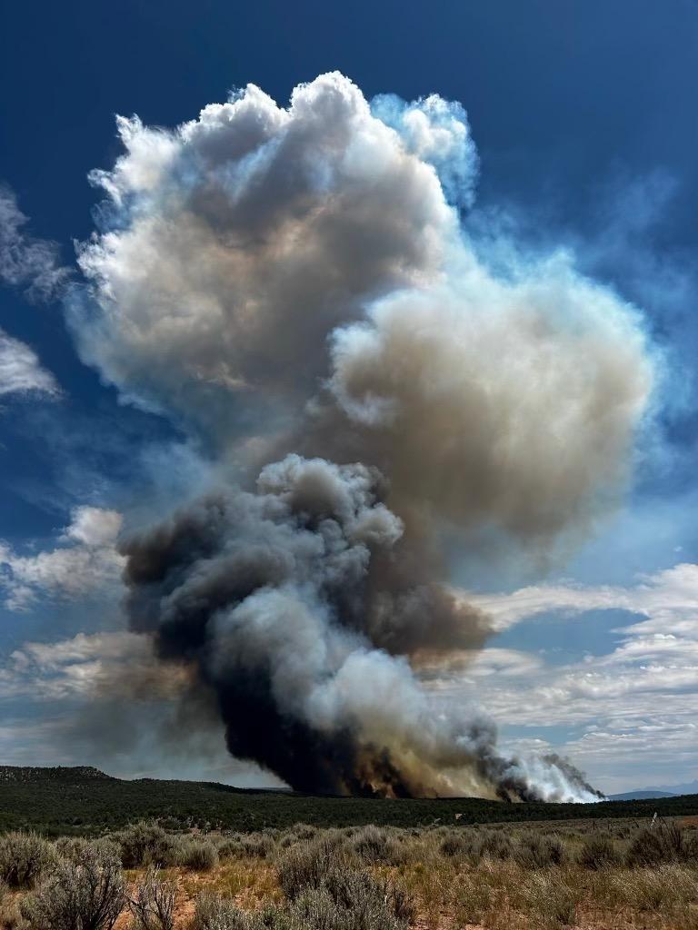 The photo shows a large, black smoke column rising up from a flat, desert landscape