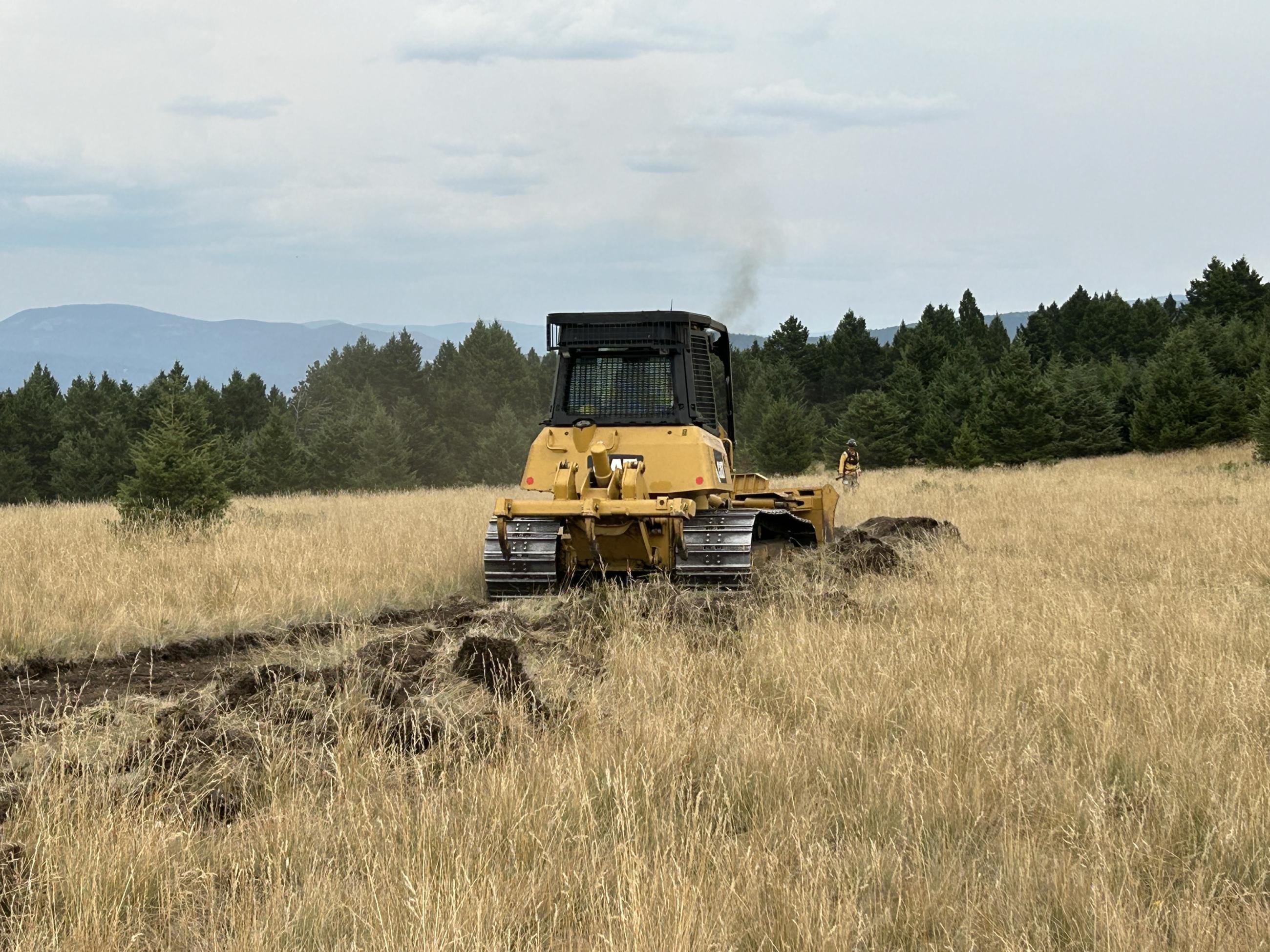 A heavy equipment boss walks in front of a bull dozer, directing him where to doze line.