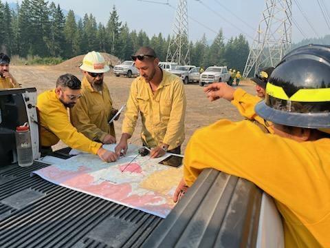 Firefighters wearing yellow gather around a truck bed looking at a map