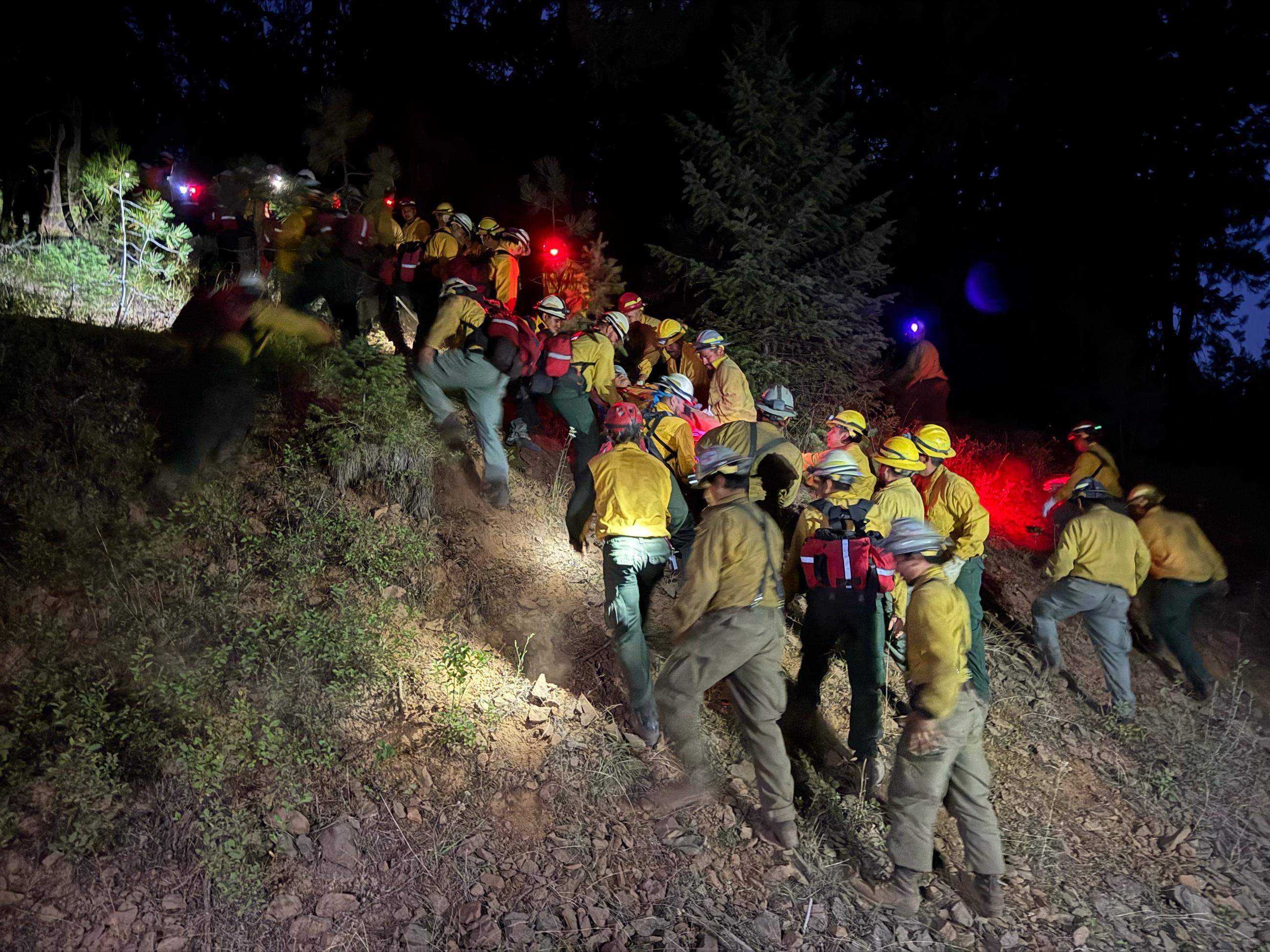 A team of firefighters practice making a chain and brining a person on a litter down a mountain side.