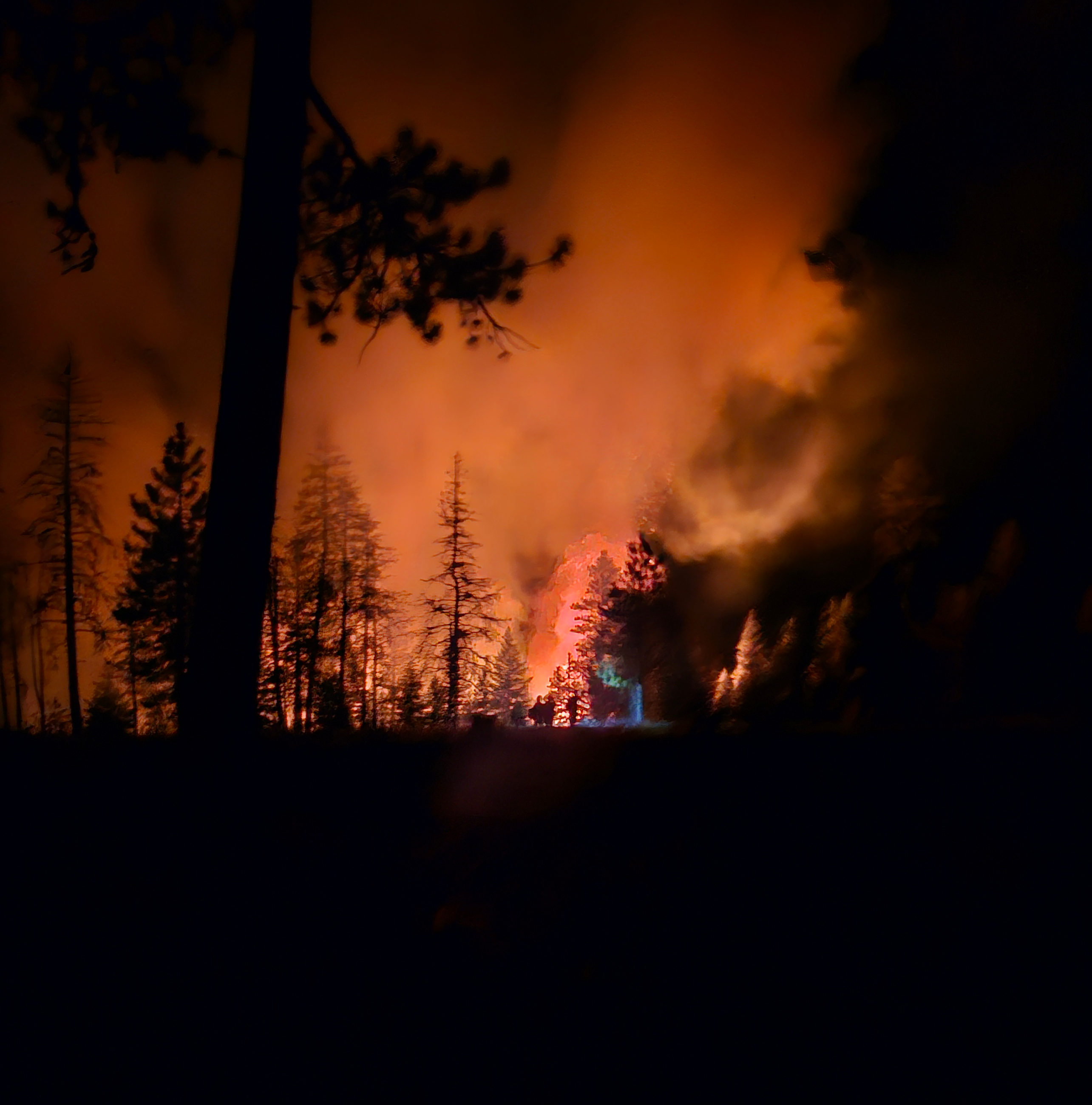 The light from a firefighters helmet shines from the center of a sky glowing with orange smoke.