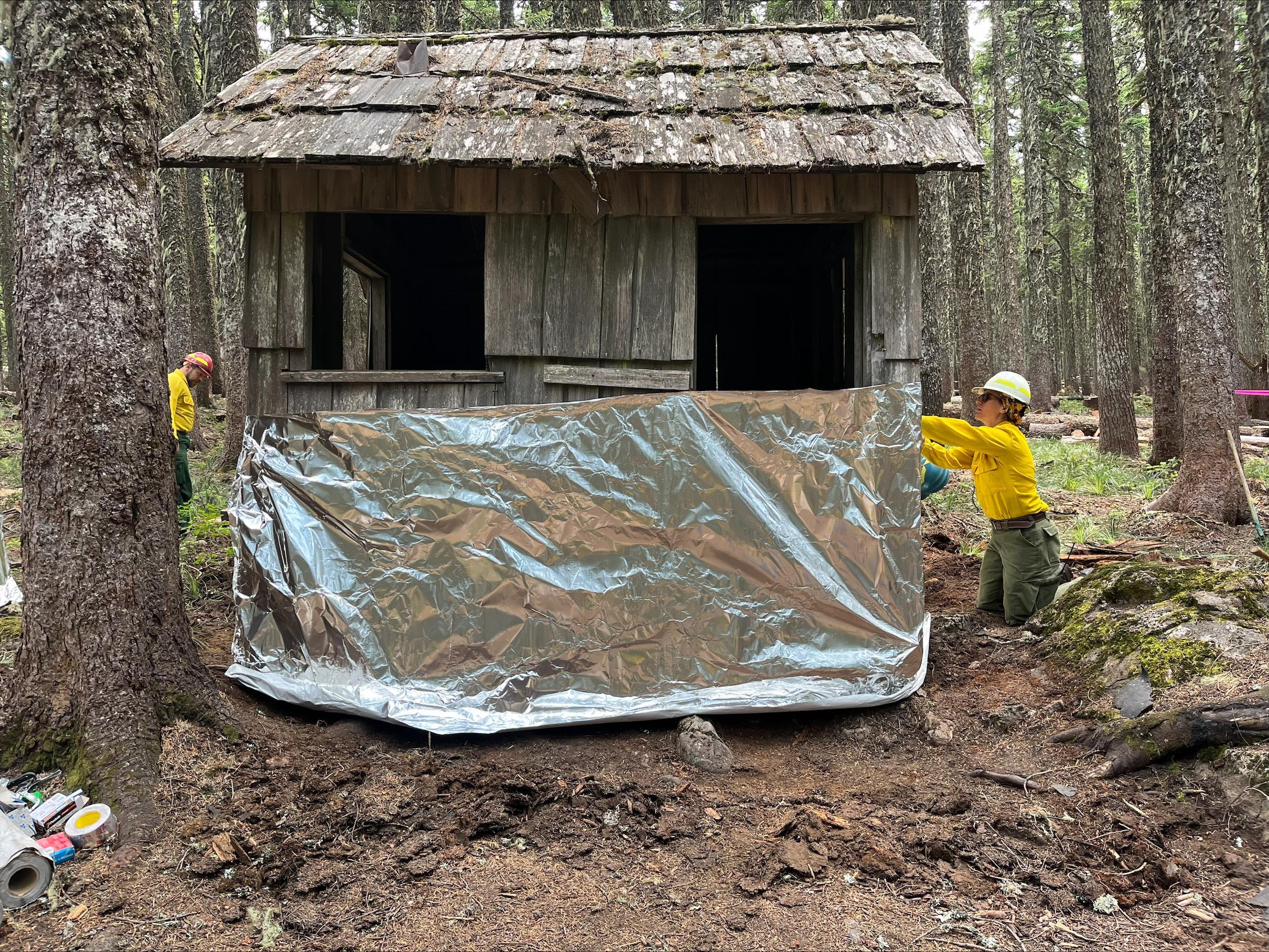A small cabin with no window or door is half covered with silver wrappings