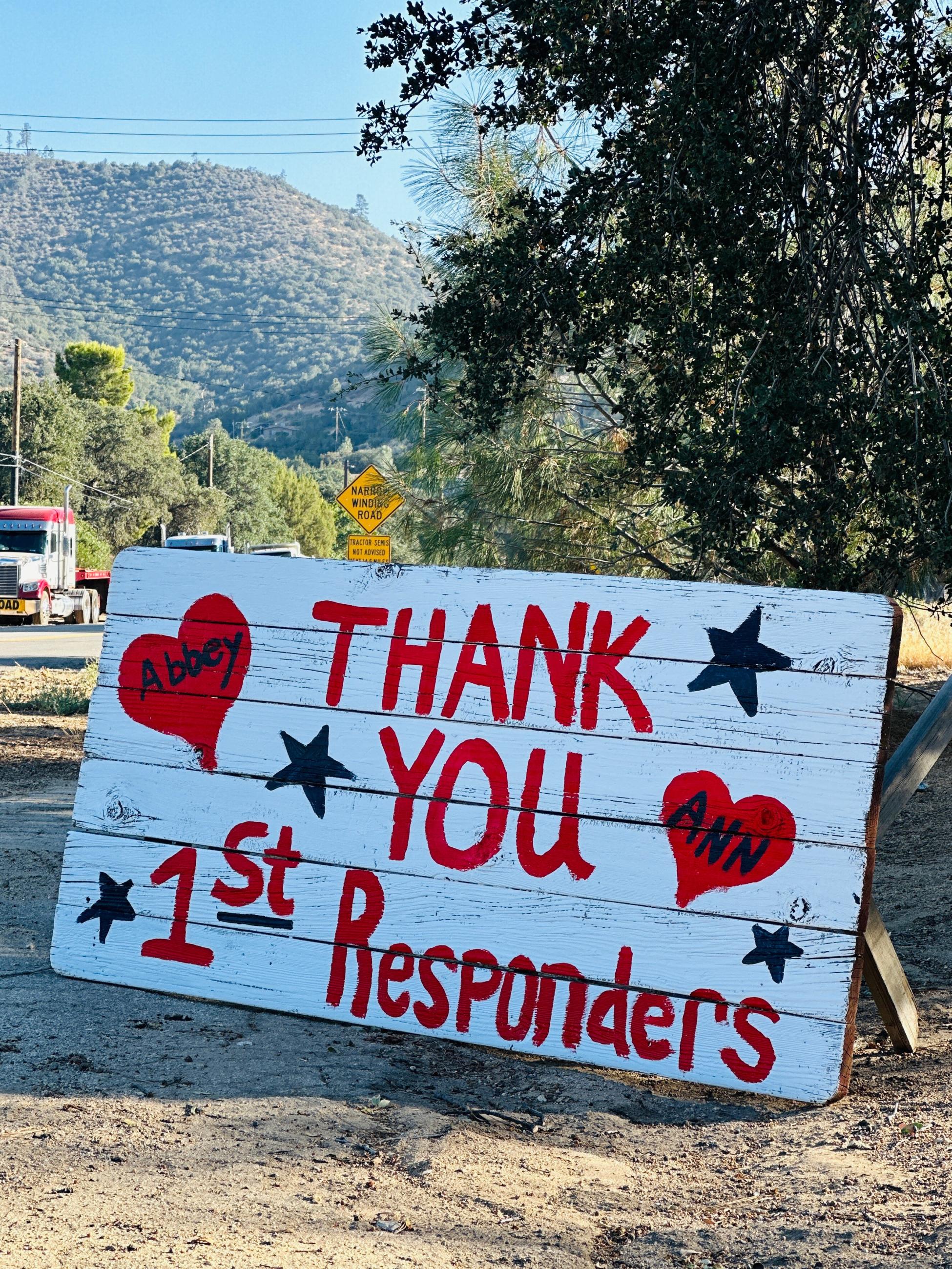 A white wooden signs has painted red letters that read thank you 1st responders, from Abbey and Ann
