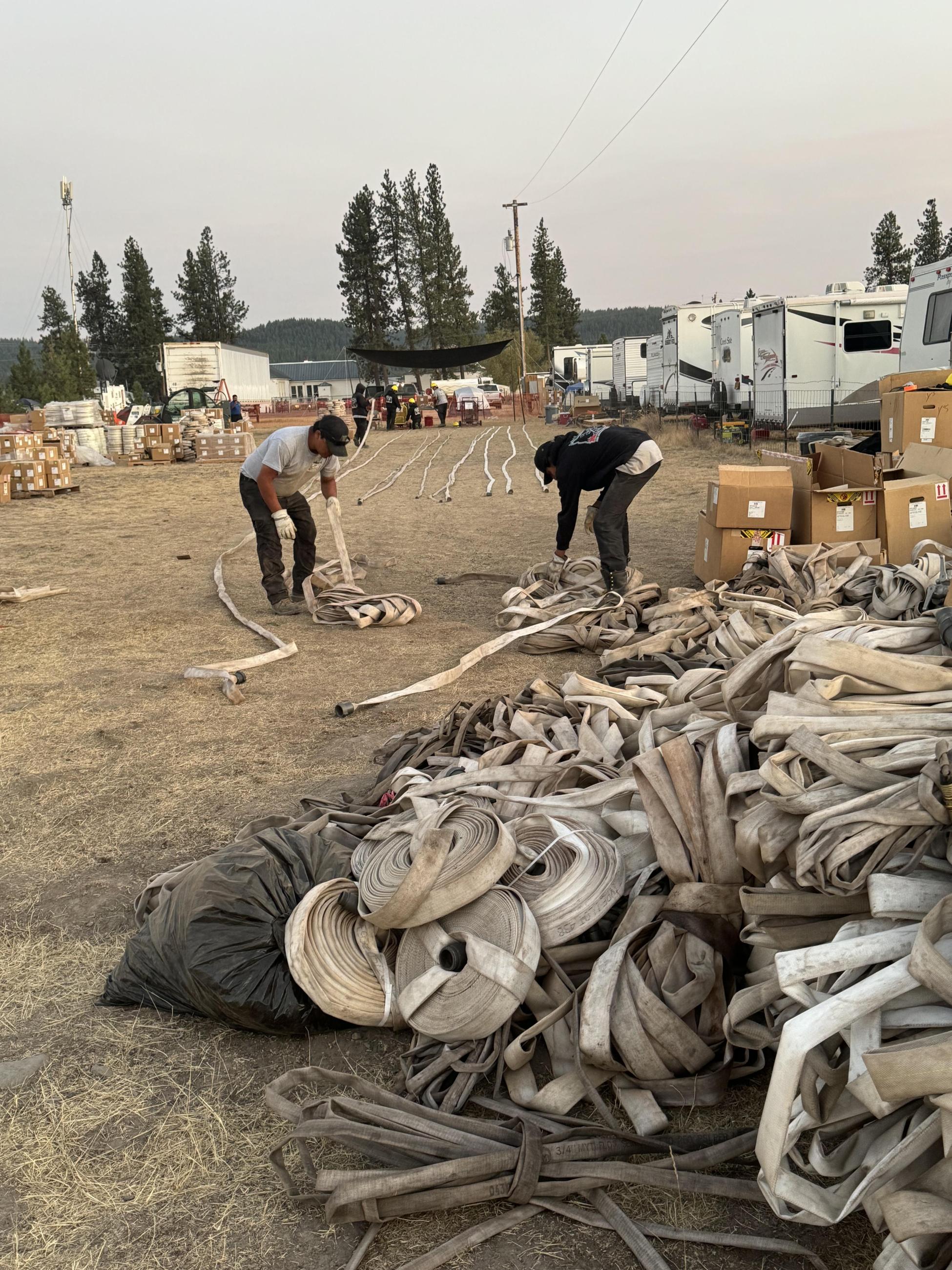 Two men stand in front of long lines of fire hose. In front of them is a large pile of hose.