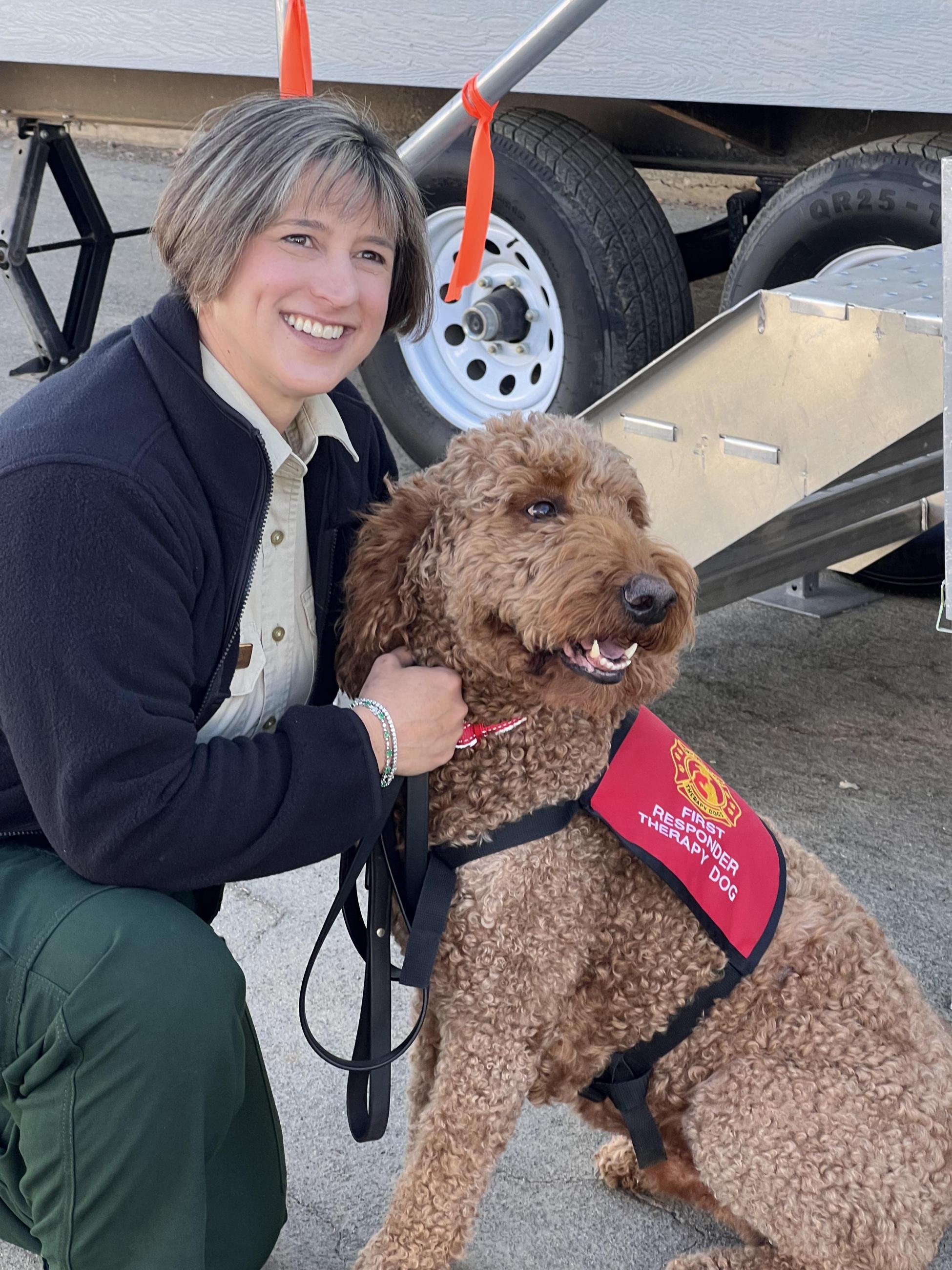 A smiling female US Forest Service employee pets a therapy dog