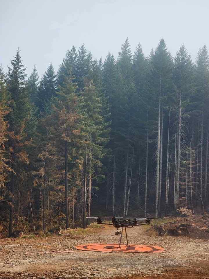 A UAS sits on orange pad in forest clearing