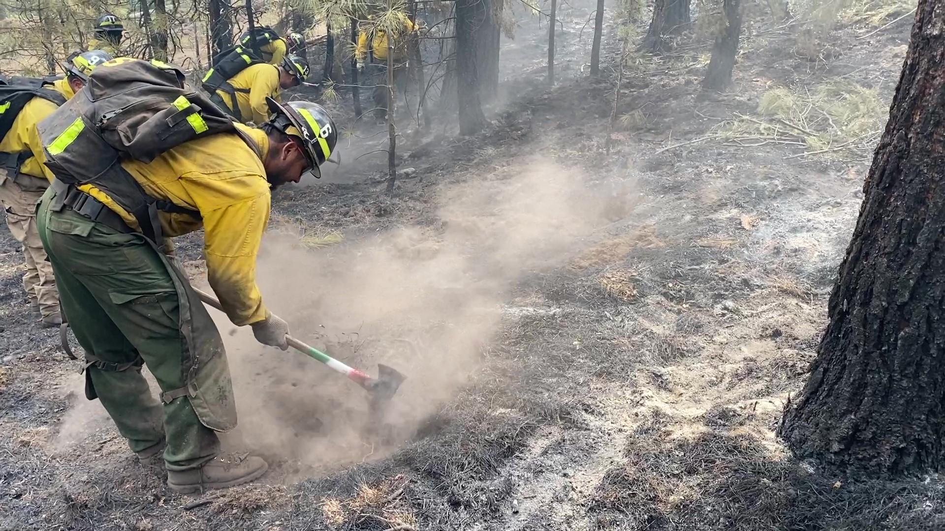 Crew member using a hand tool to dig into black charred ground. 