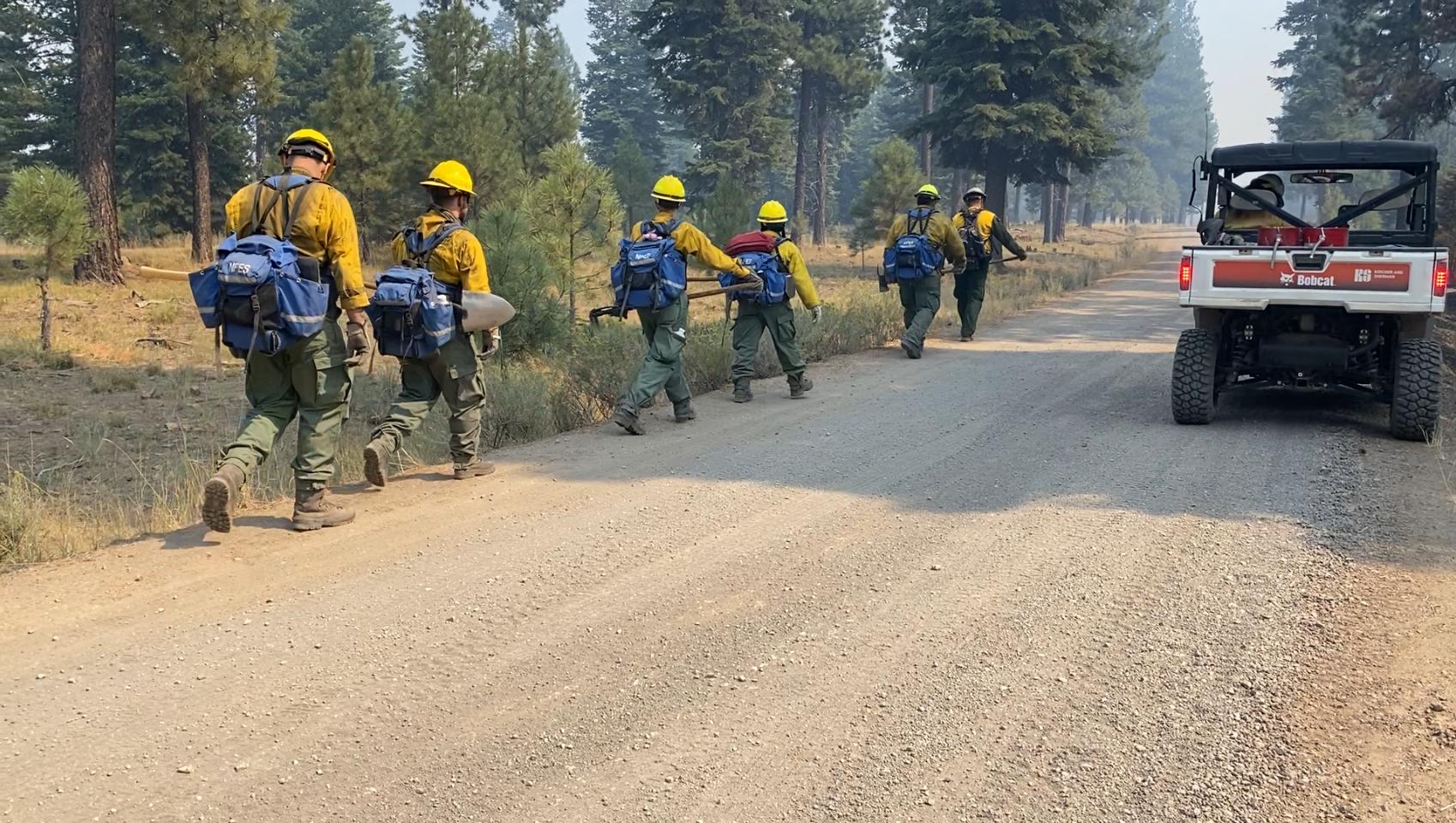 Firefighters walk in line along the road on the Falls Fire