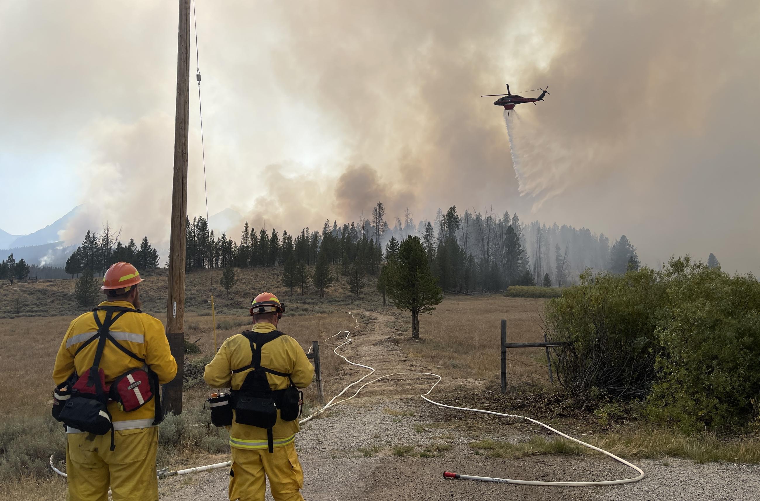 firefighters watch as helicopter drops water on spot fire