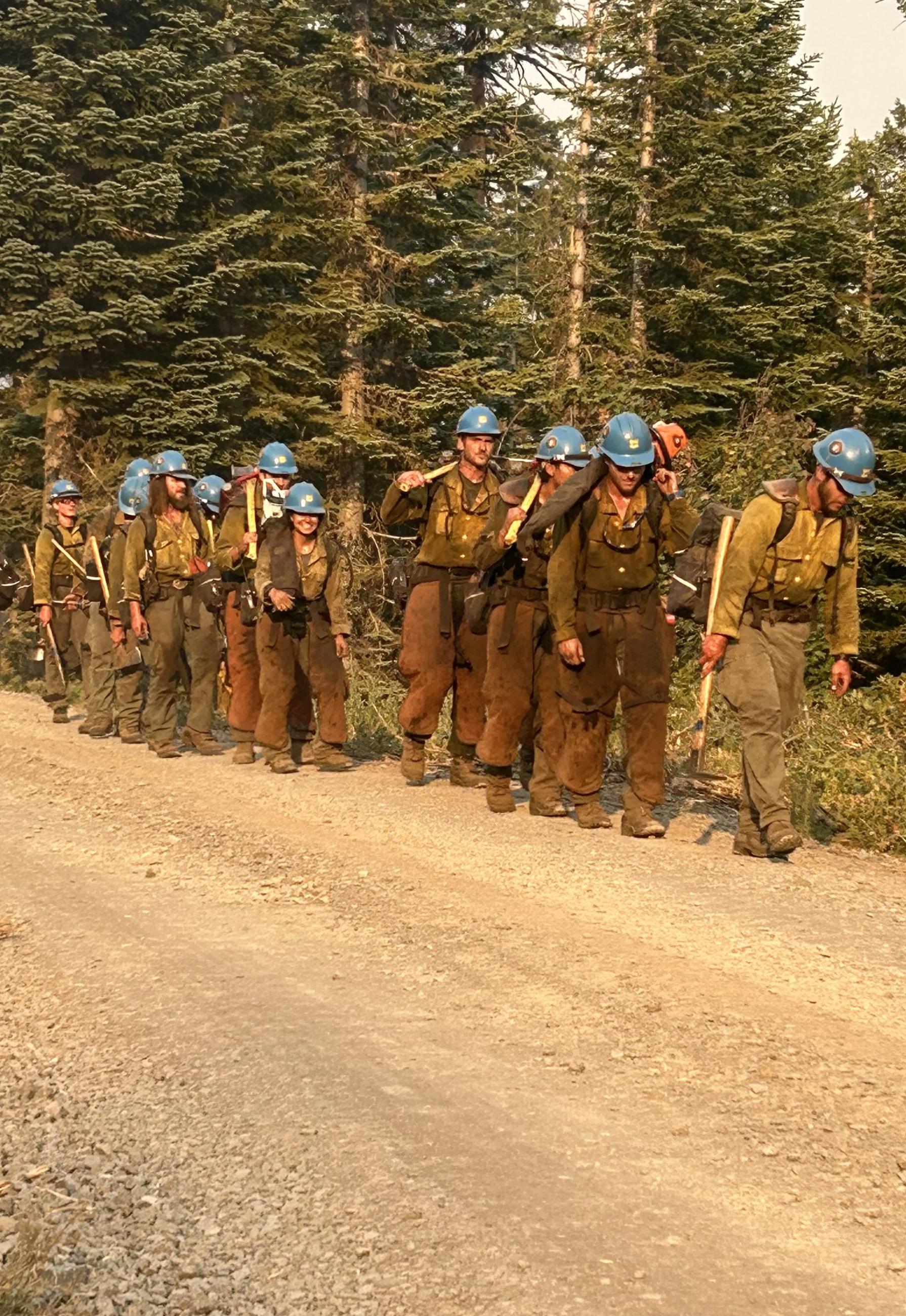 Firefighters with blue helmets walk a road at end of the day