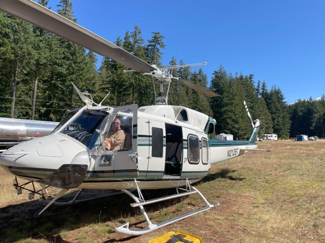 Picture of a Bell 212 Helicopter. It is white with a blue stripe down the side.