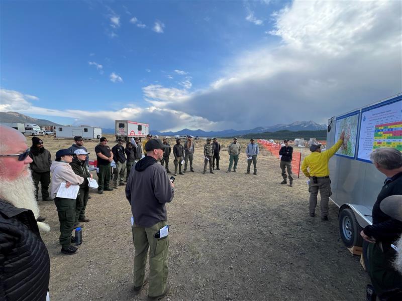 Firefighters form a circle and look at a map at night shift briefing, sunday, aug 25