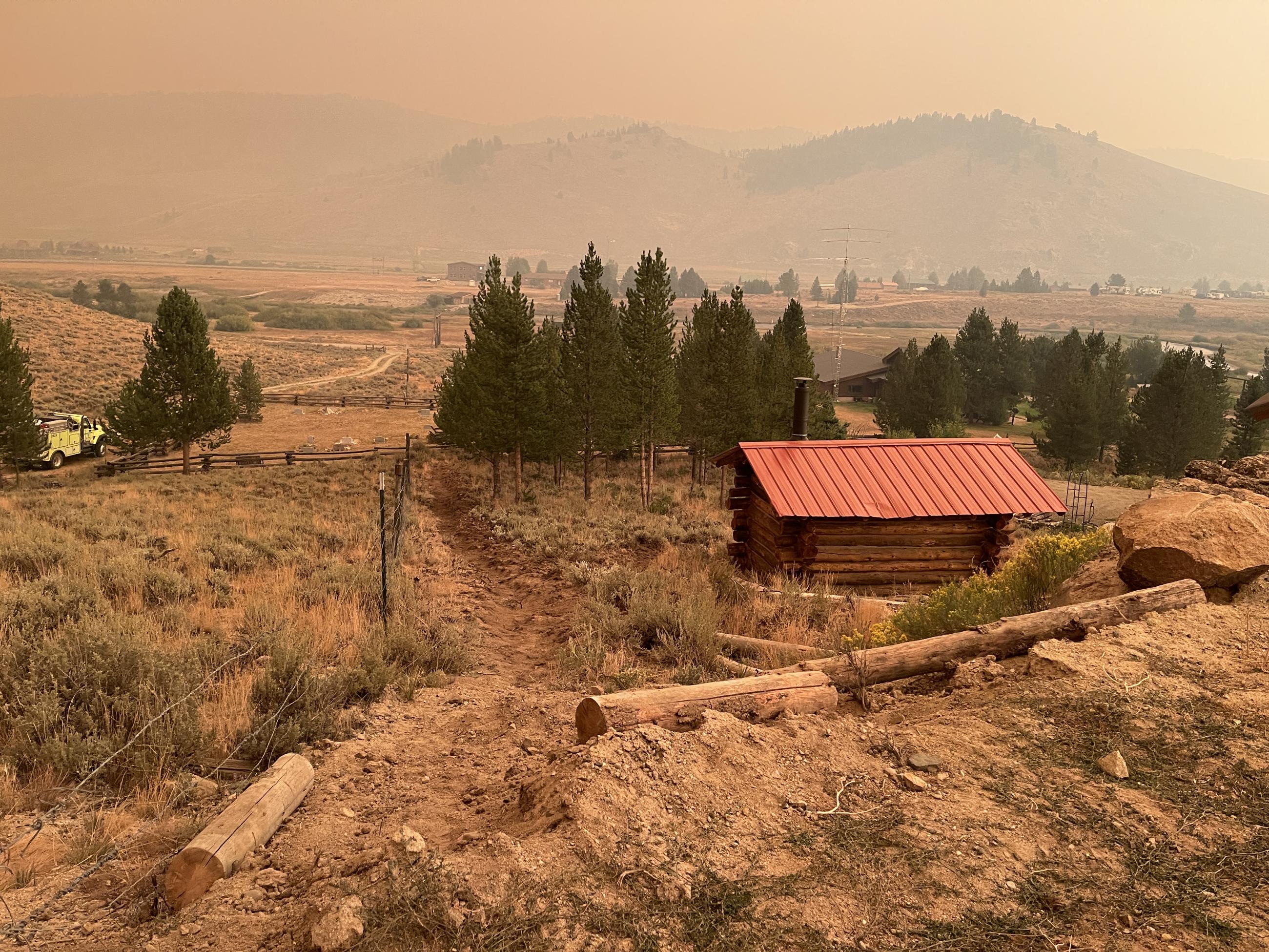 a fireline dug by a hand crew along a fence next to a cabin on a steep slope overlooking Stanley, 8/28