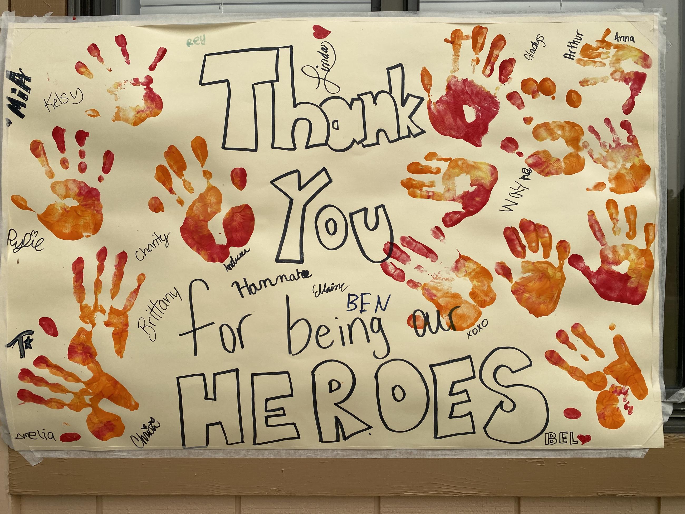 Handmade sign that says Thank You for being our heroes and has colorful handprints signed by childern who made the sign. 