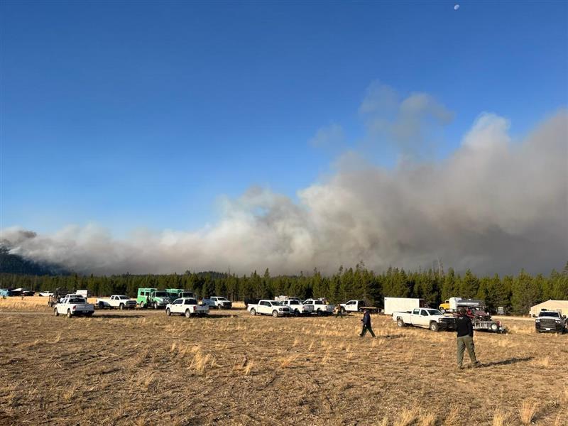 Fire personnel take down yurts and prepare to move to new command post as fire moves closer. Large column in background Friday, 8/23