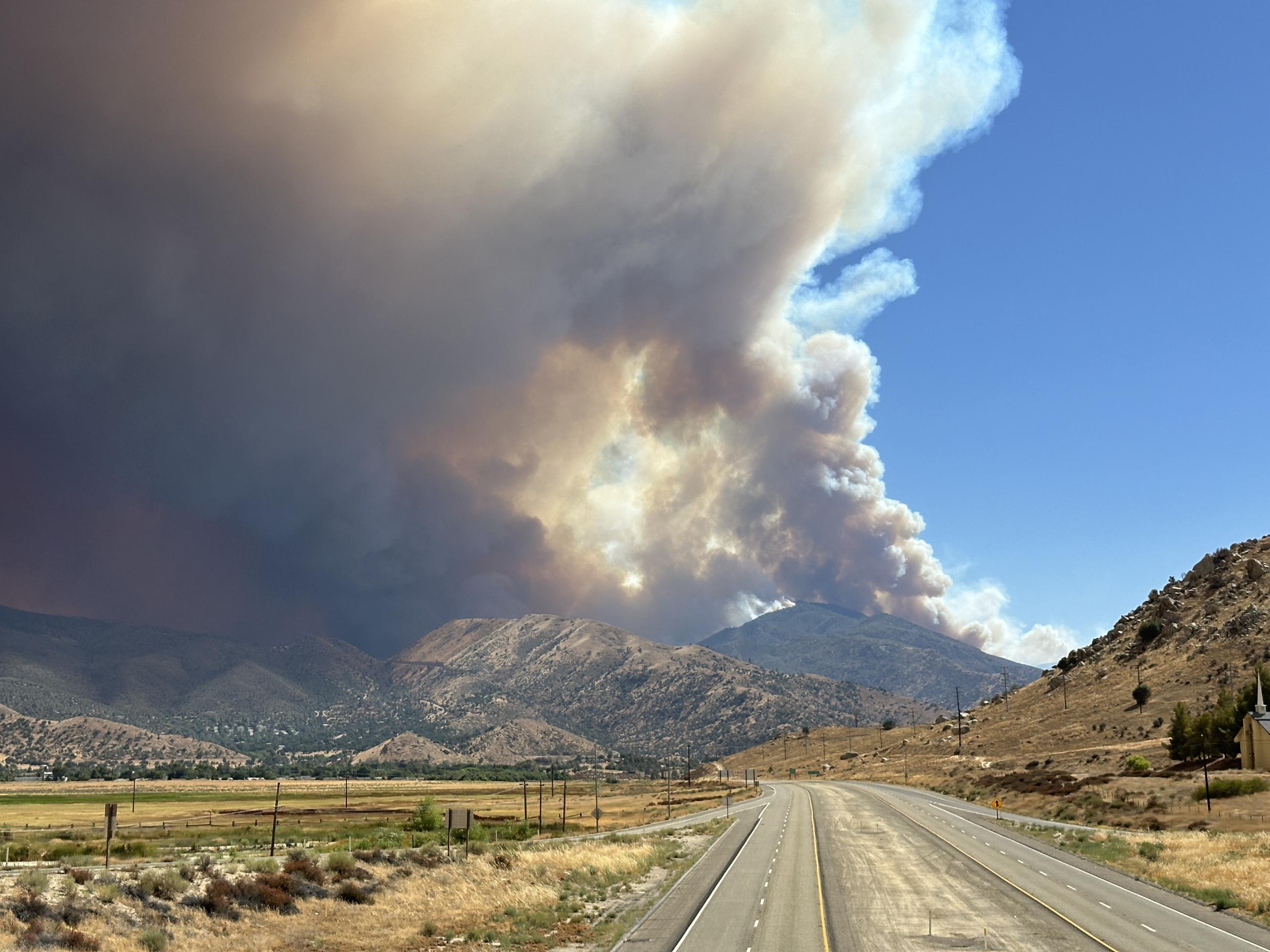 The frame is largely made up of a column of smoke, with a little blue sky in the upper right hand corner. the foreground is a road through the desert