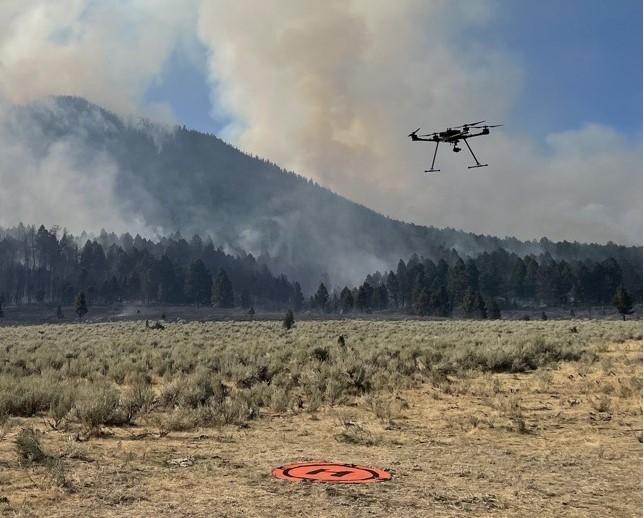 Drone flies from its landing pad to conduct firing operations, leaving from a sagebrush meadow and moving to the forest.