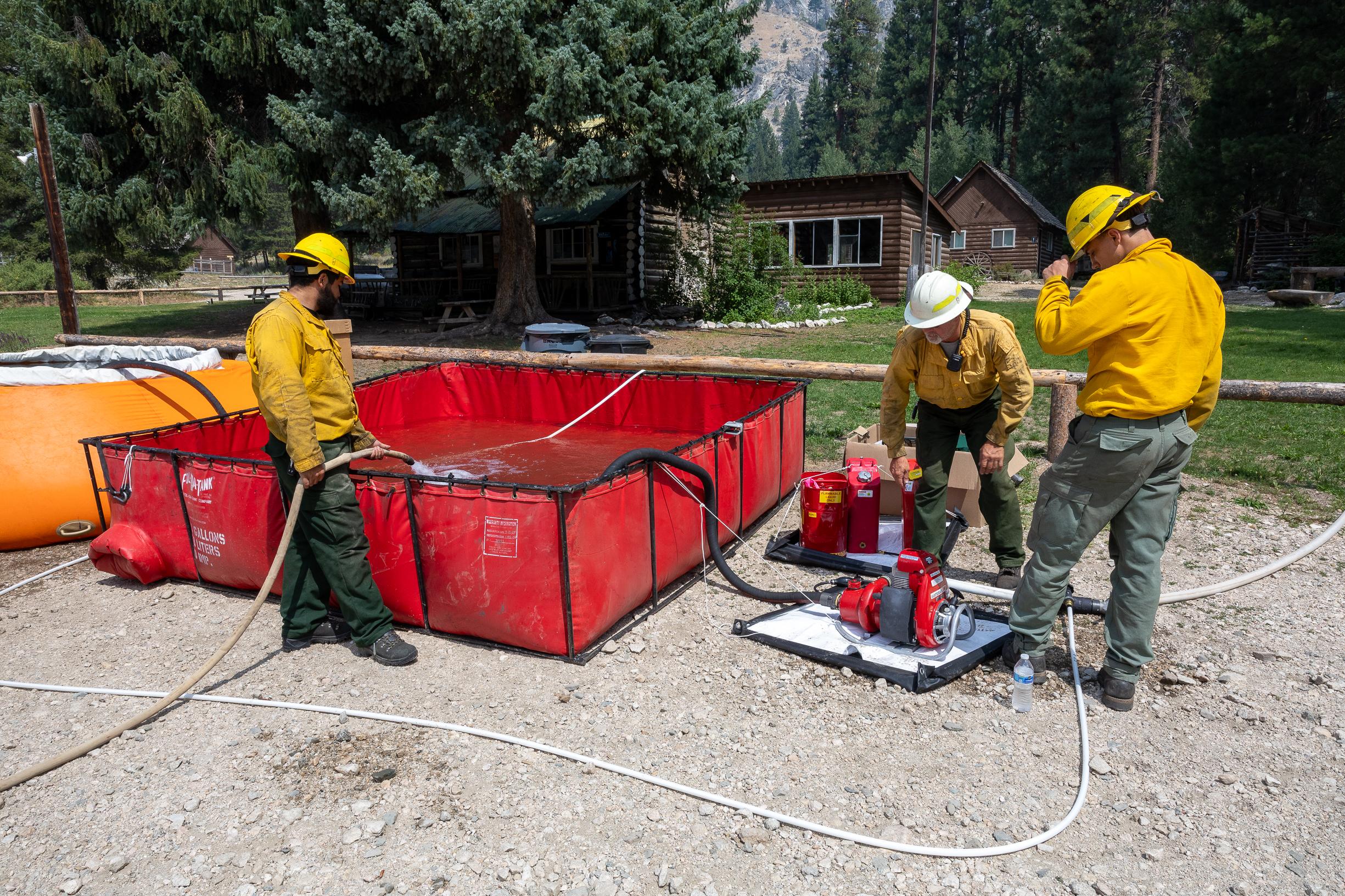 Picture displays three firefighters setting up a portable water tank for point protection.