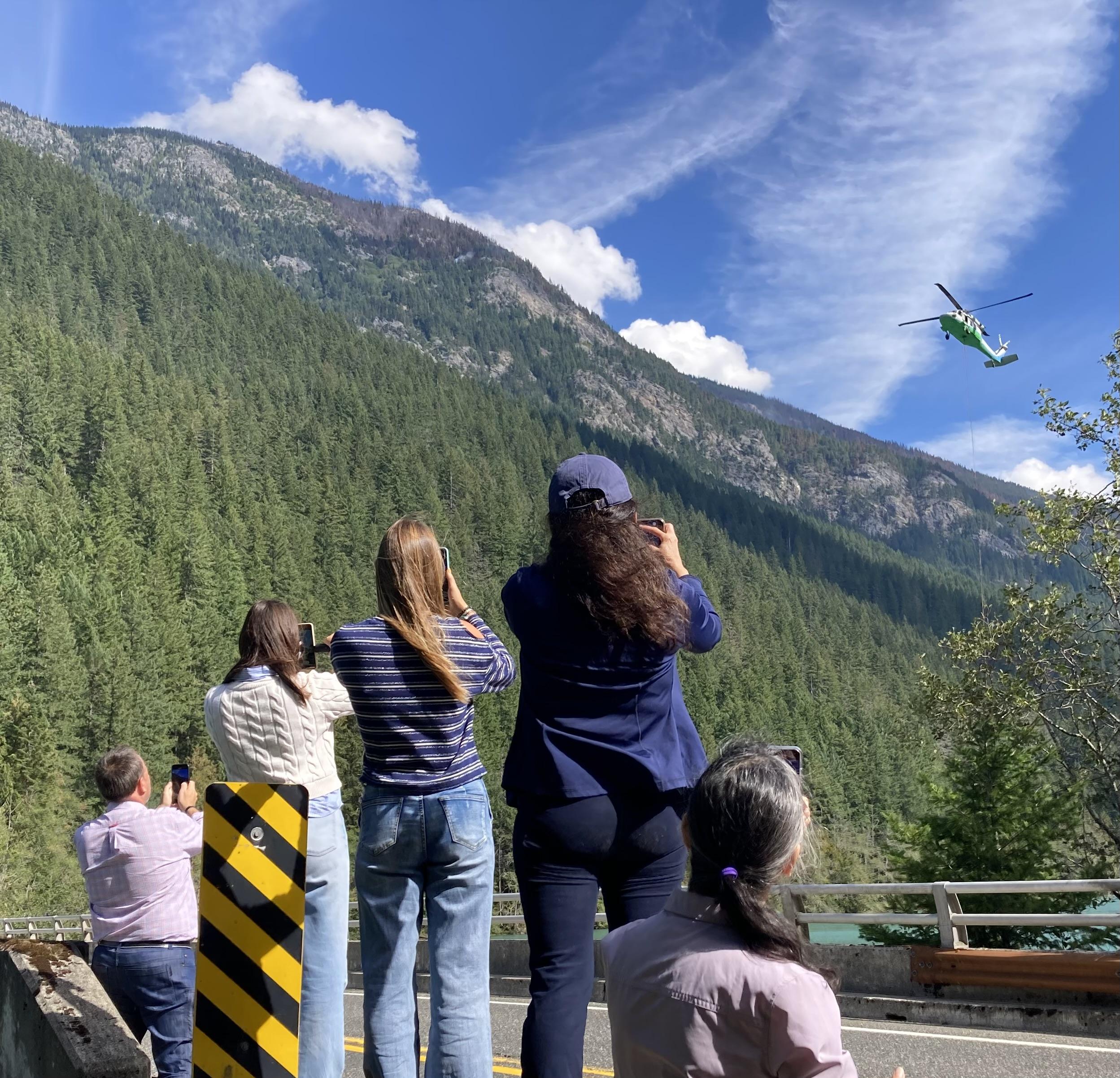 Visitors watch a helicopter pull water for the Ruby Fire