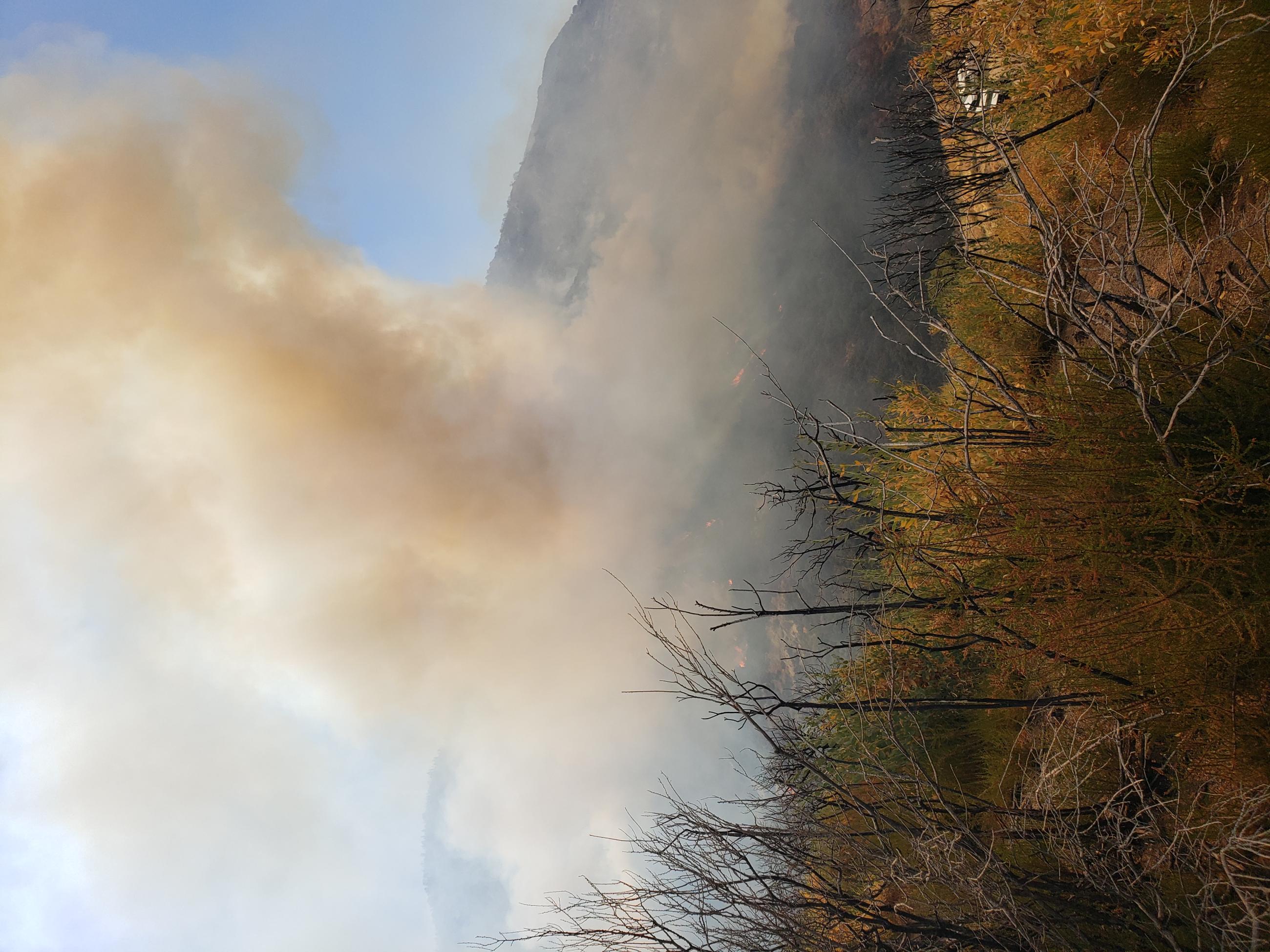 A large dark smoke column rises above the landscape. 