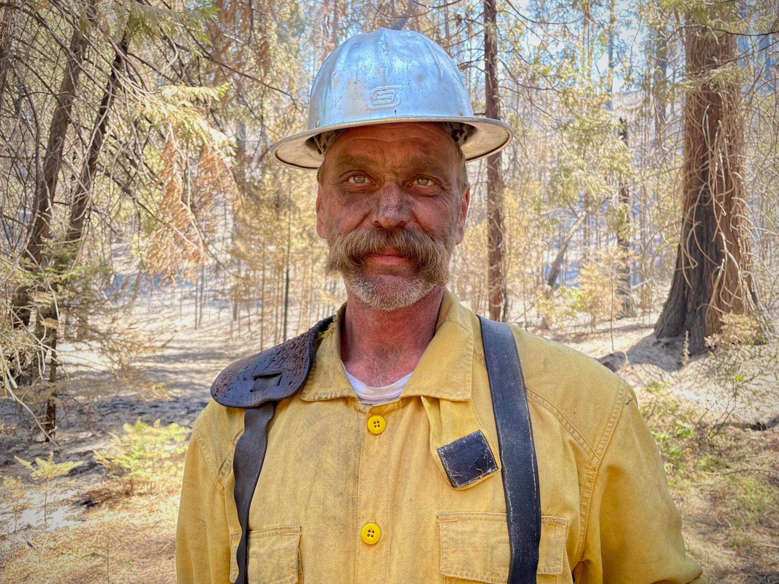 A firefighter in yellow with gray helmet looking at the camera. 