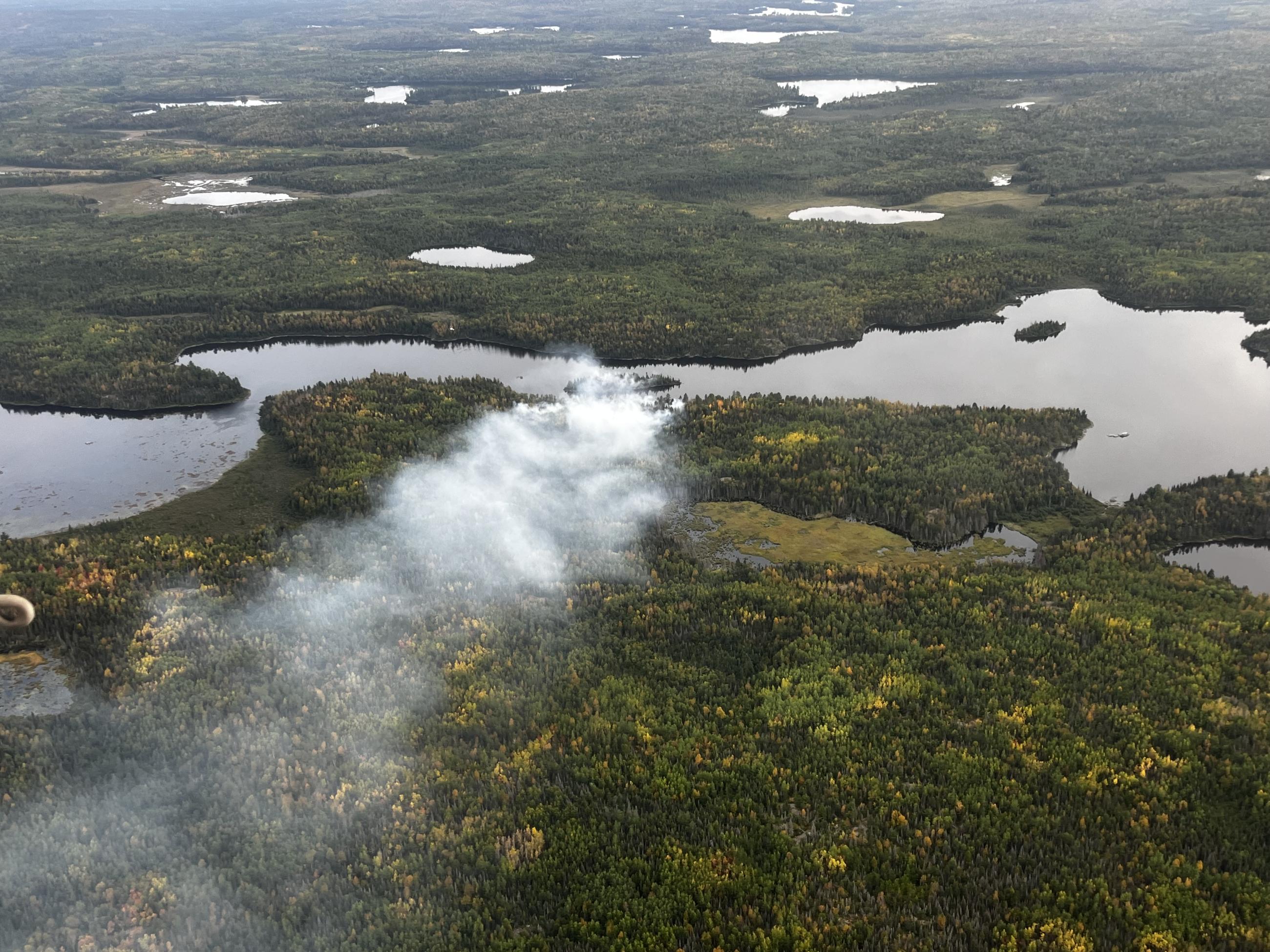 Image of a wildfire and smoke from the area across a lake and forest landscape