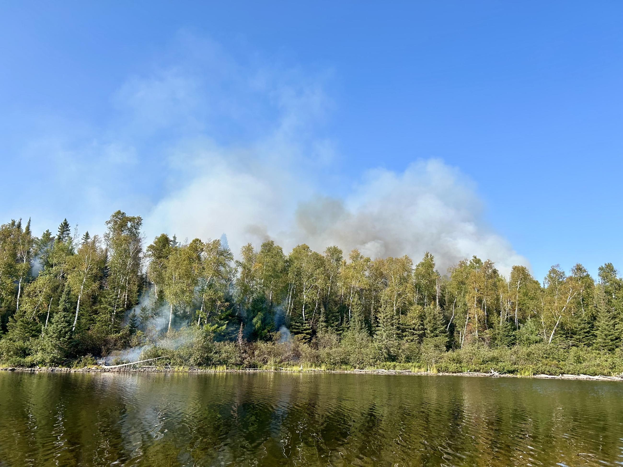 Smoke rises from land by a lake 