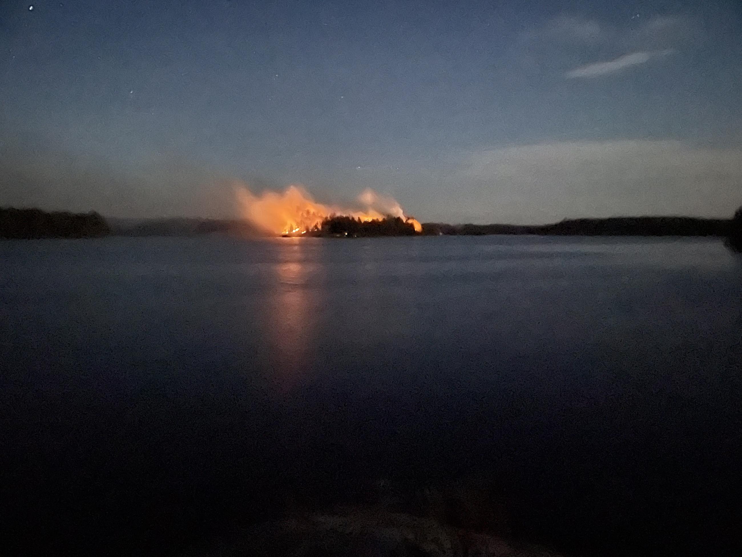 Orange wildfire flames in the distance across a lake