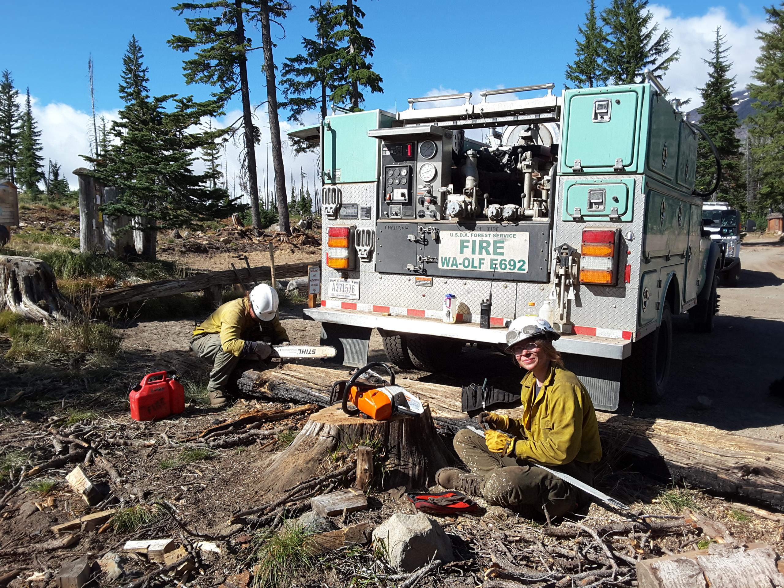 Two female firefighters are sitting by their fire engine while they do maintenance work on chainsaws.