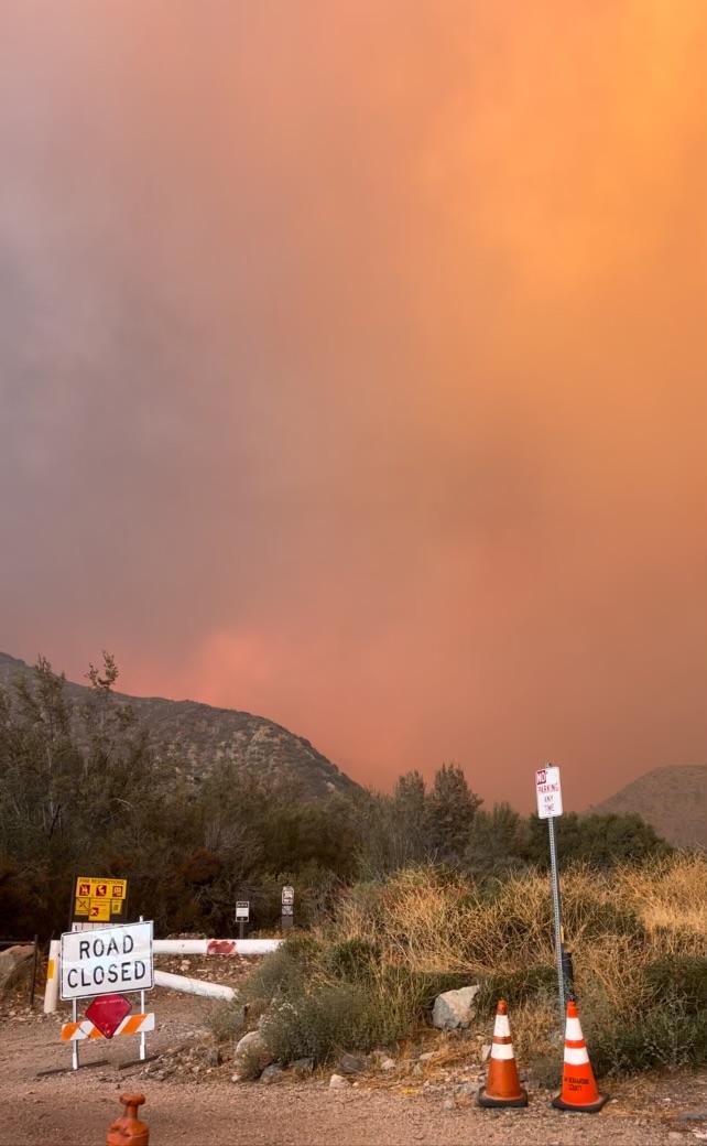 A smoky orange sky and hillside are the background for a road closed sign 