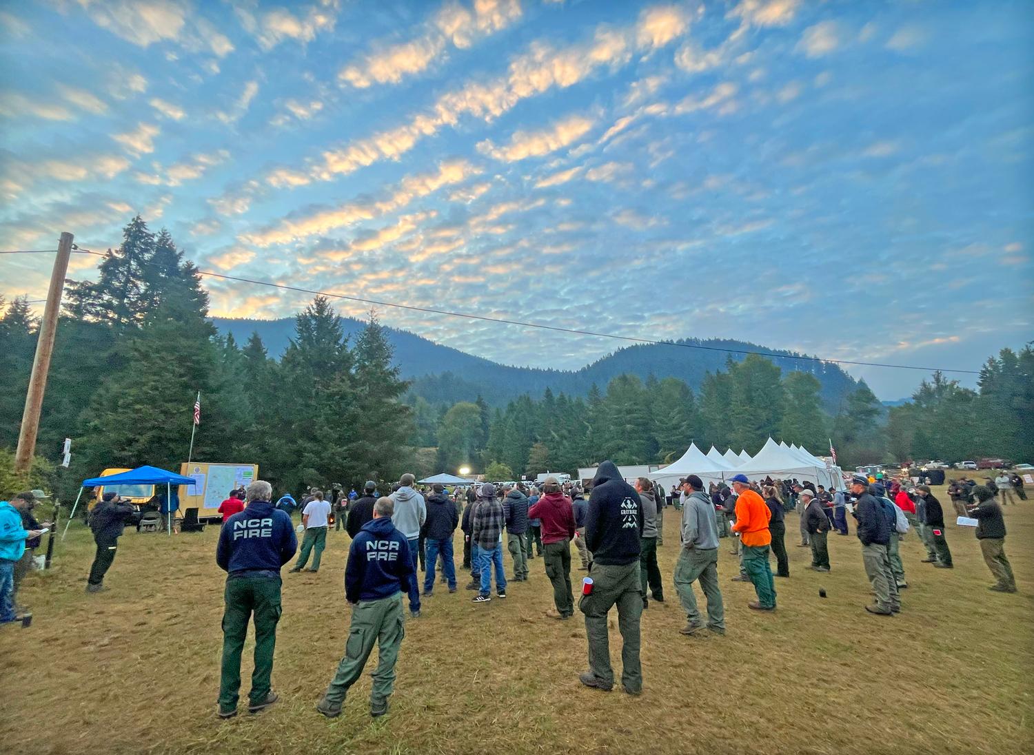 A group of firefighter stand facing a stage used for morning briefing with pillowing clouds above their head.