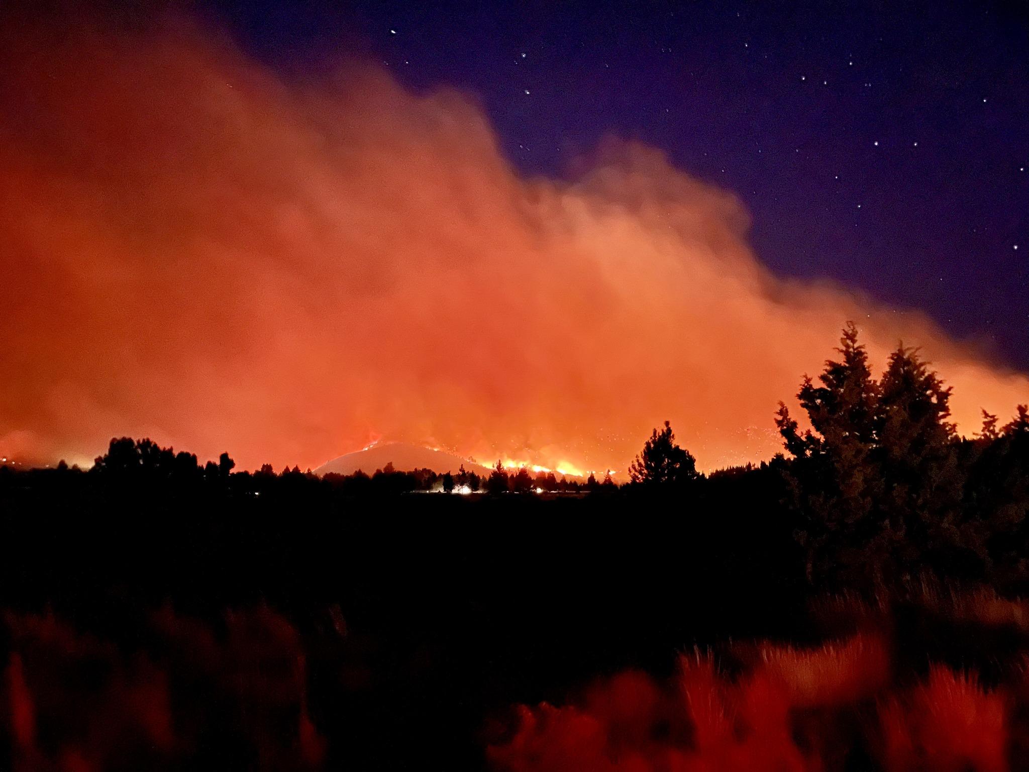 A orange and red glow above flames on a ridge with a night sky in the background. 