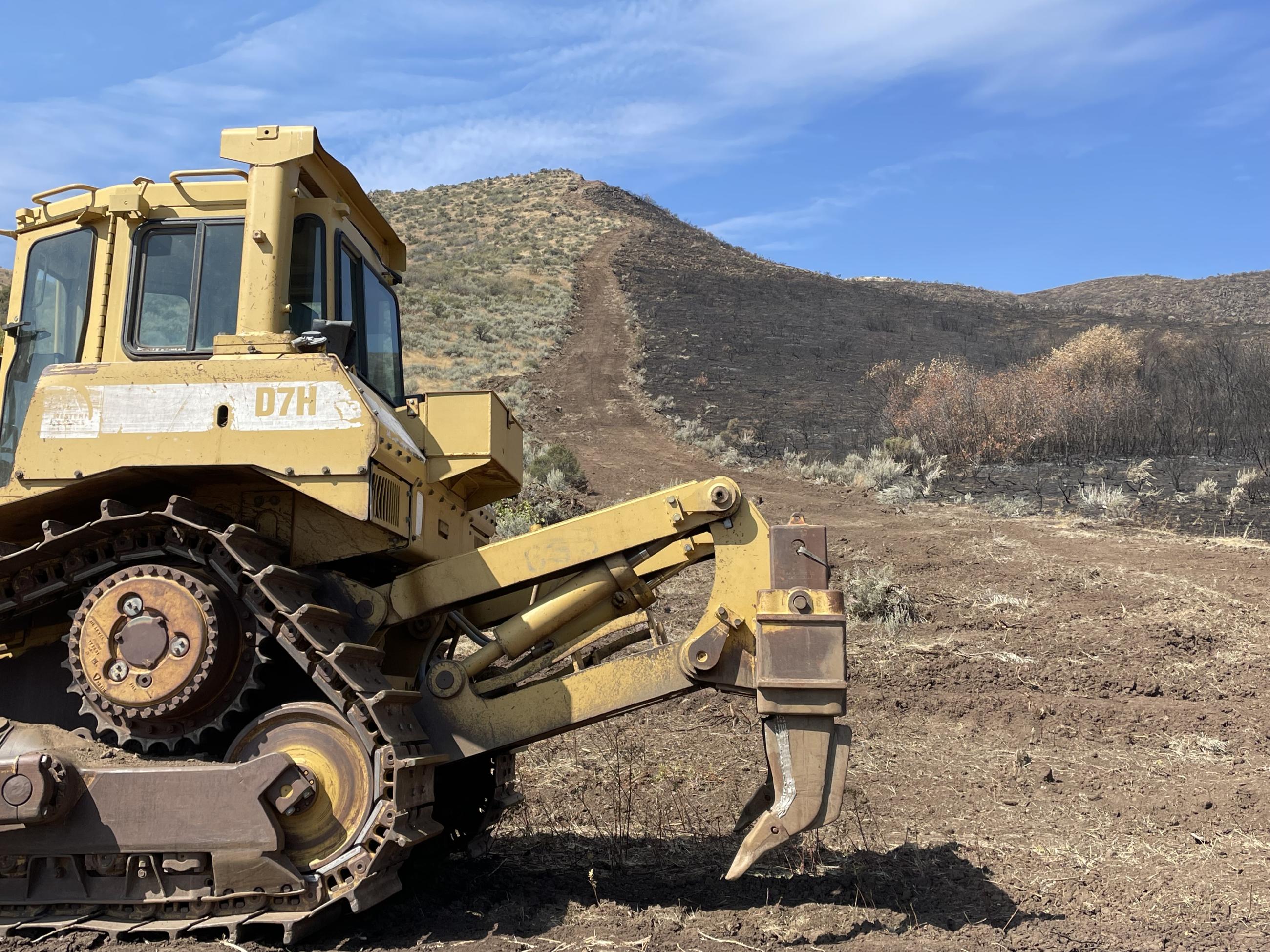 Large yellow bulldozer sitting near a hillside with black fire line.